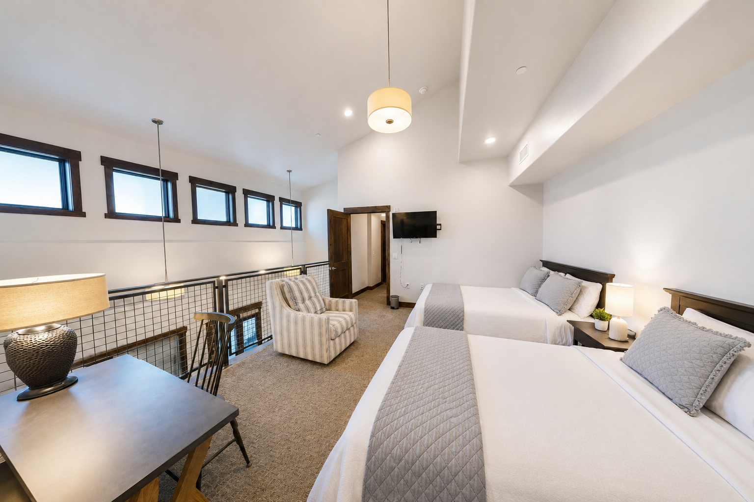 Relax in this bright and spacious bedroom featuring two plush queen beds, vaulted ceilings, and an integrated workspace. This versatile retreat offers a cozy armchair and modern art accents, perfect for families or groups.