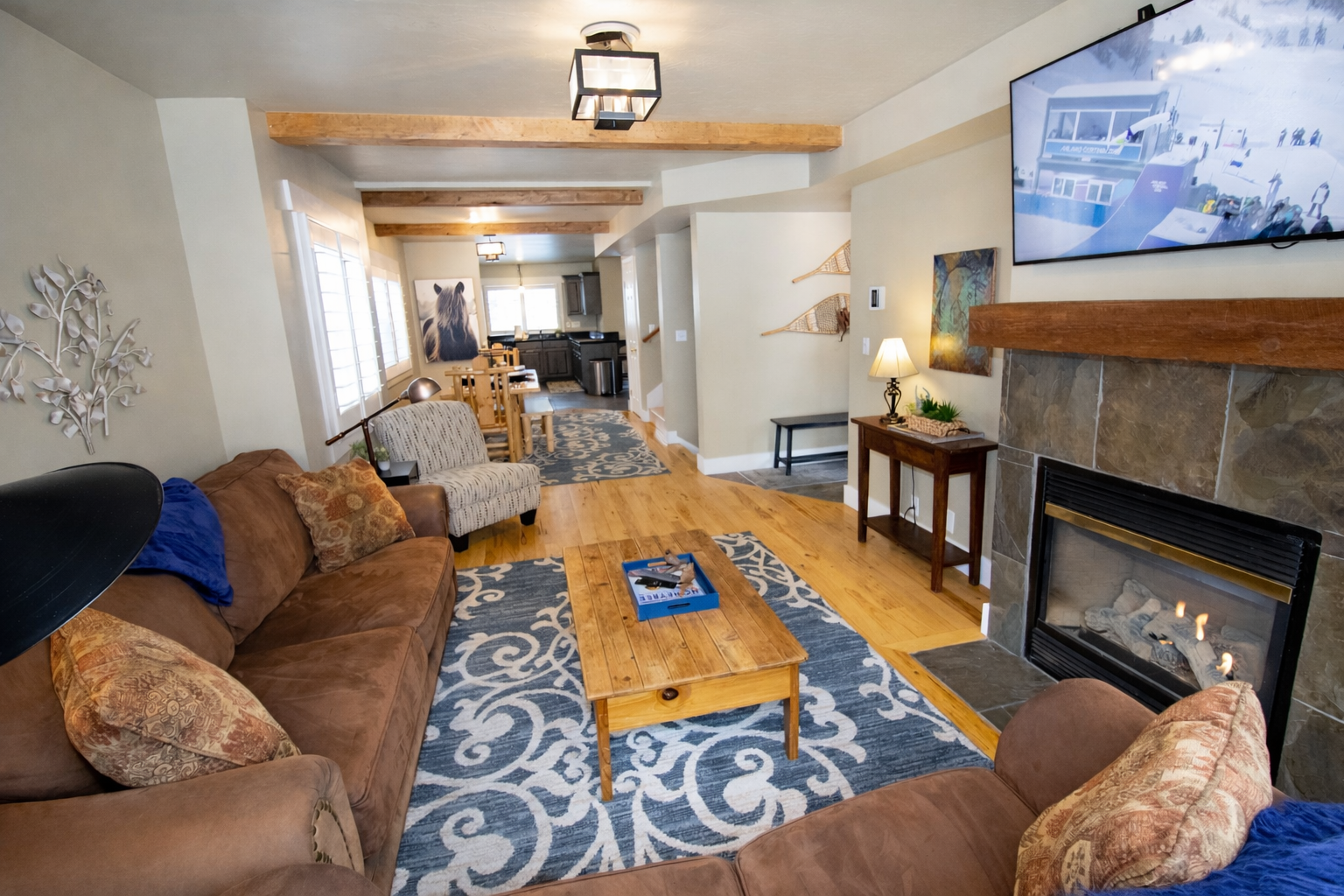 Relax in this cozy mountain retreat featuring a warm fireplace, rustic wooden accents, and plush seating. Enjoy modern amenities like a wall-mounted TV and large windows with bright, natural light.