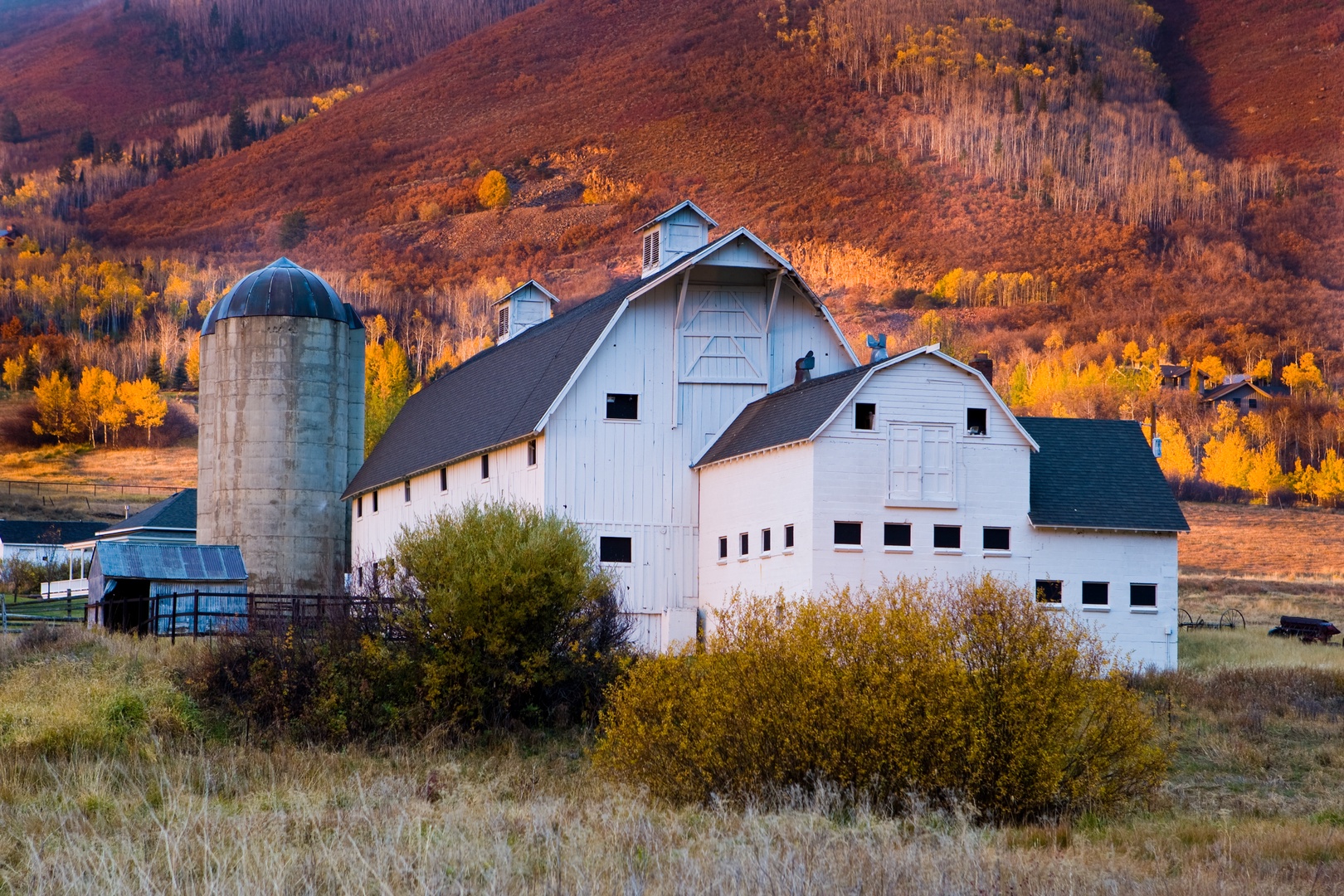 Historic barn property nestled in scenic mountain valley with vibrant autumn foliage creating a picturesque rural setting.