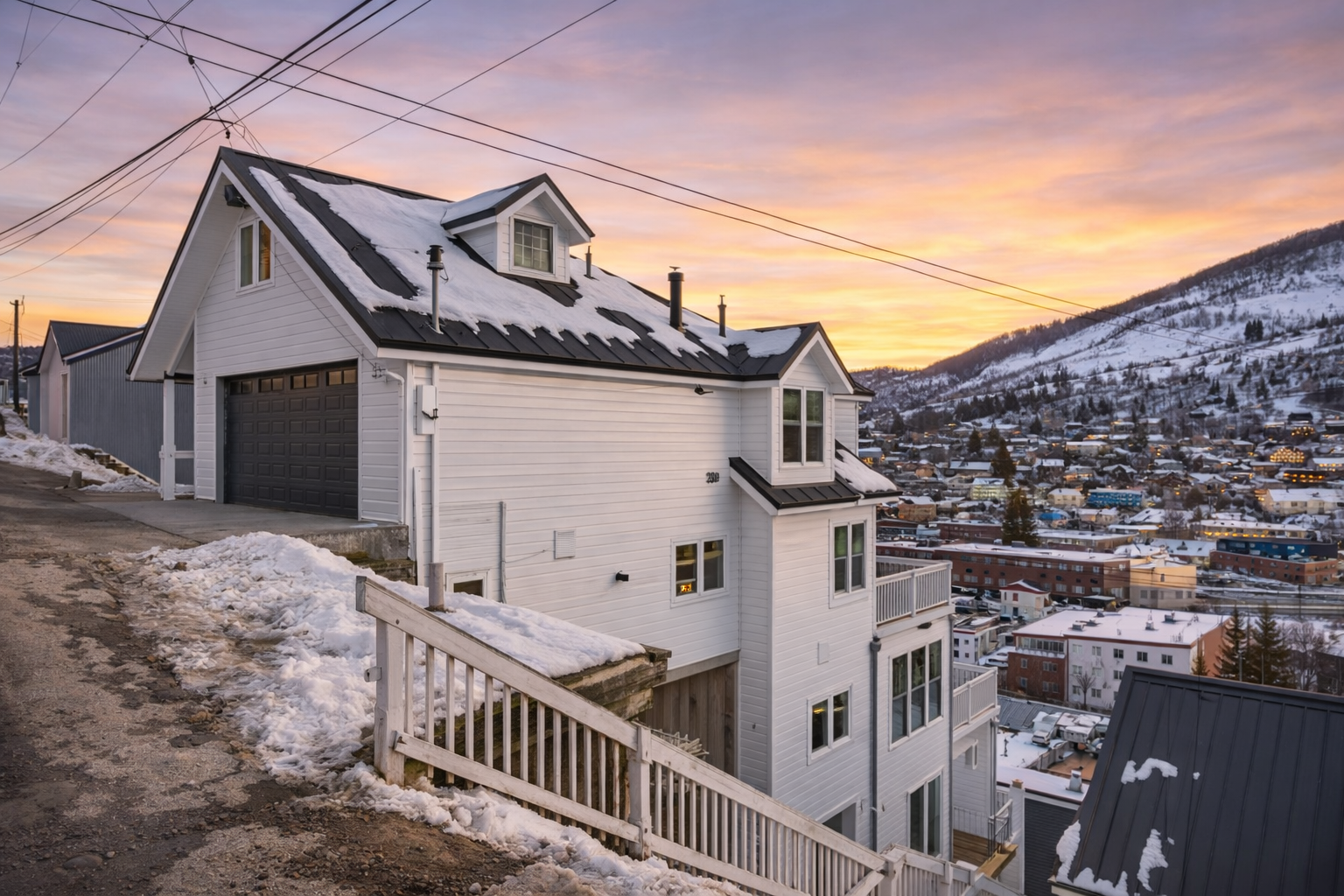 Modern mountain property overlooking a picturesque snow-covered town, perfectly positioned for stunning valley views during golden hour.