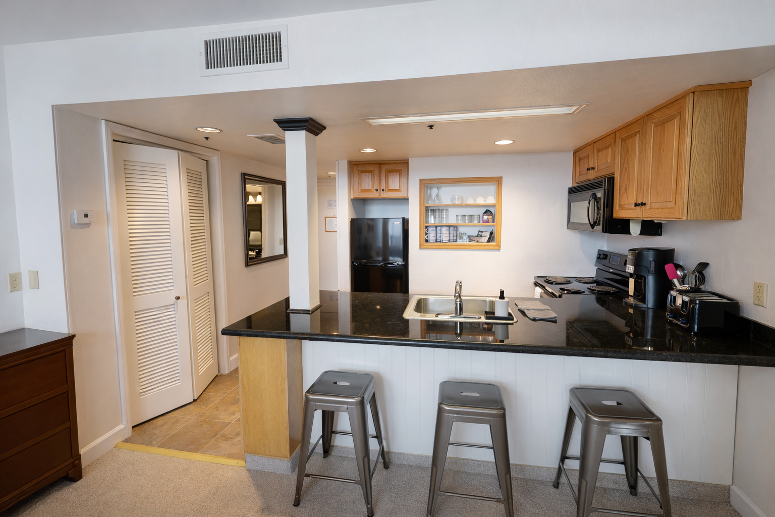 Your sleek kitchen features gleaming black granite countertops, modern appliances, and a breakfast bar perfect for morning coffee or casual meals with friends.