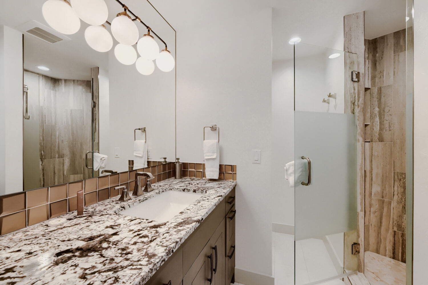 Step into your private retreat with marble-topped vanities, elegant bronze fixtures, and spa-inspired wood-look tile. The oversized mirror and soft globe lighting create a warm, welcoming glow that's perfect for unwinding after a day of adventure.