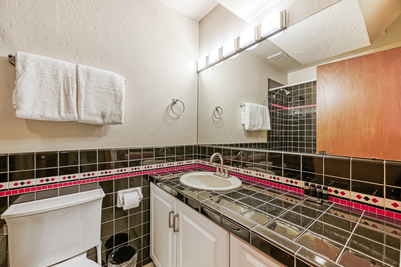 Bright and freshly stocked, this bathroom features gleaming tile work with a stylish accent stripe, fluffy towels ready for your use, and a welcoming warmth that helps you unwind after a day of adventure.