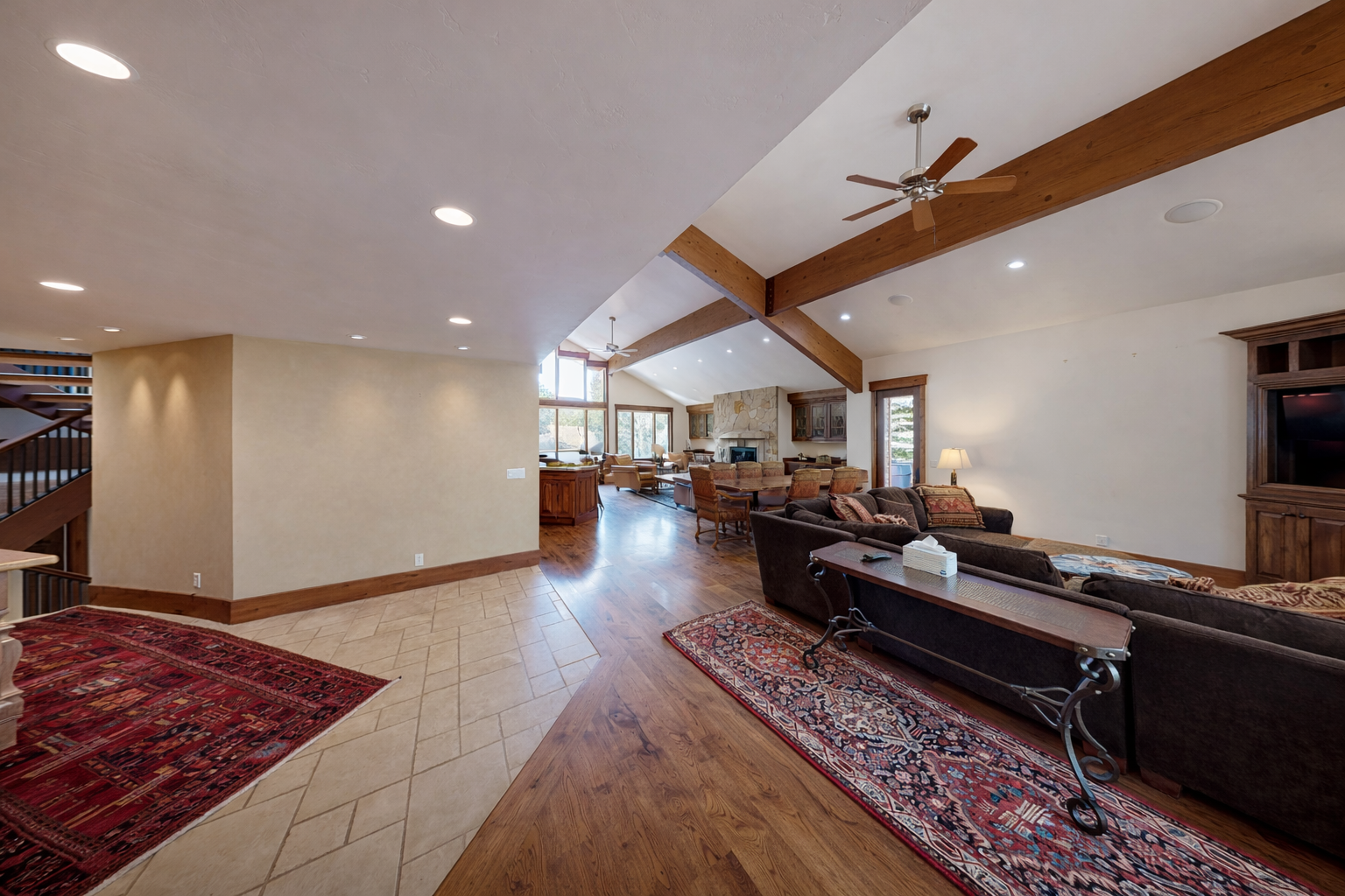 Relax in our spacious great room with a vaulted wood ceiling, exposed beams, and a cozy fireplace area in the distance.