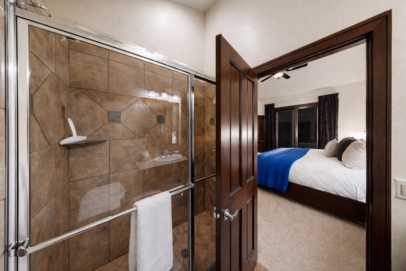 Step from your luxurious tiled shower into your cozy bedroom sanctuary, where rich wood accents and plush bedding await your arrival.
