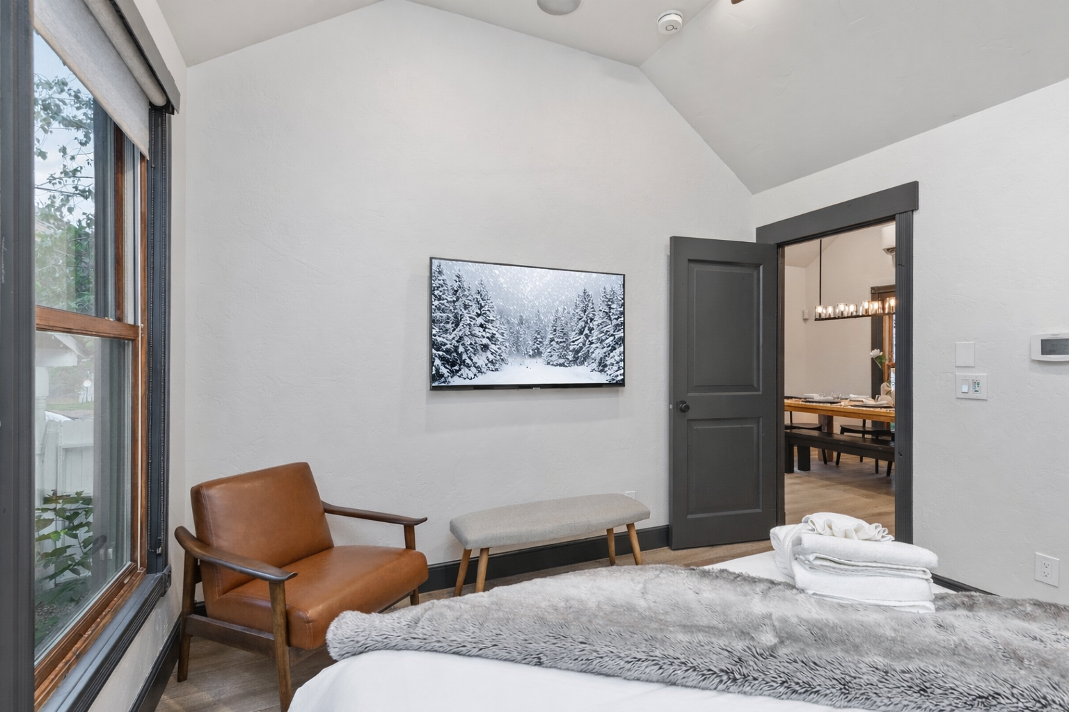 Unwind in your serene bedroom featuring soaring ceilings, warm leather seating, and peaceful forest views through expansive windows.