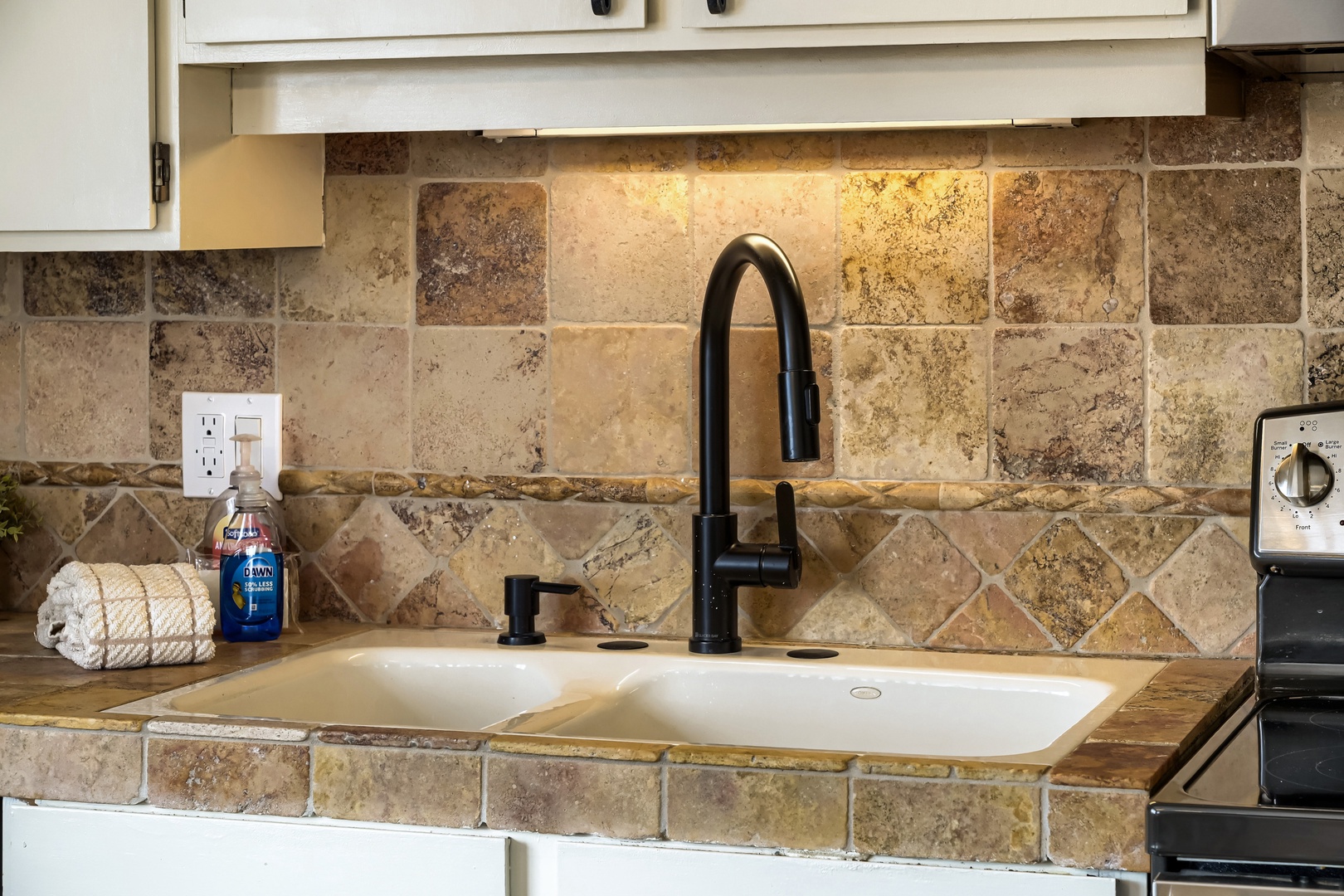 Your kitchen features beautiful stone tile countertops and backsplash, with a modern black faucet and white farmhouse sink ready for meal prep.