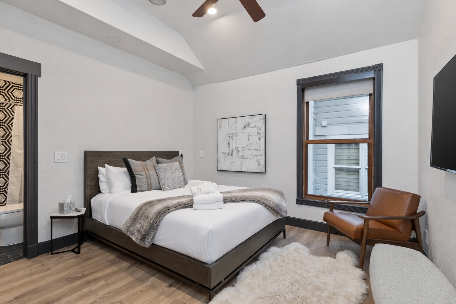 Unwind in your serene bedroom featuring soaring ceilings, warm leather seating, and peaceful forest views through expansive windows.