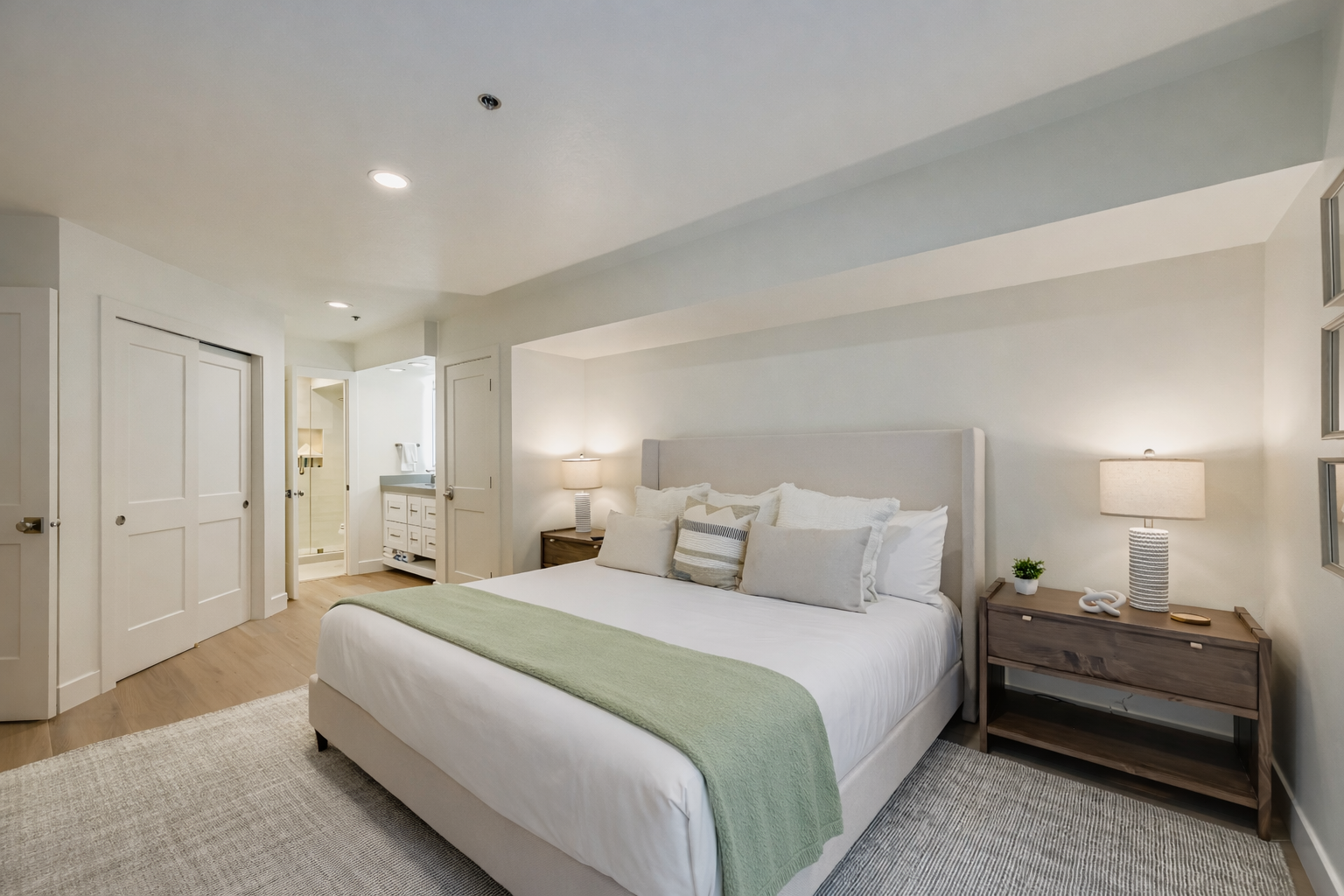 Serene primary bedroom featuring a luxurious king bed, crisp white linens, and a soft green accent throw. Modern nightstands, warm lighting, and a spacious layout create a peaceful retreat after mountain adventures.