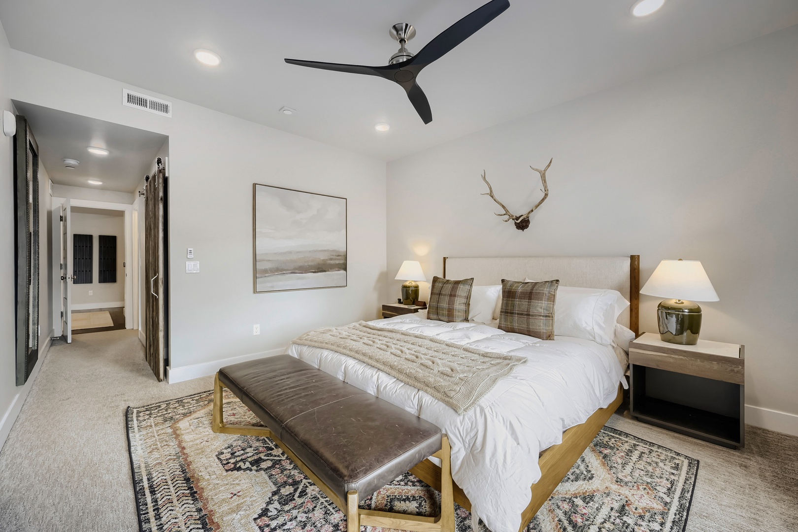 Sink into crisp linens and rustic elegance in your private bedroom retreat, where modern comfort meets mountain-inspired charm beneath a cooling ceiling fan.