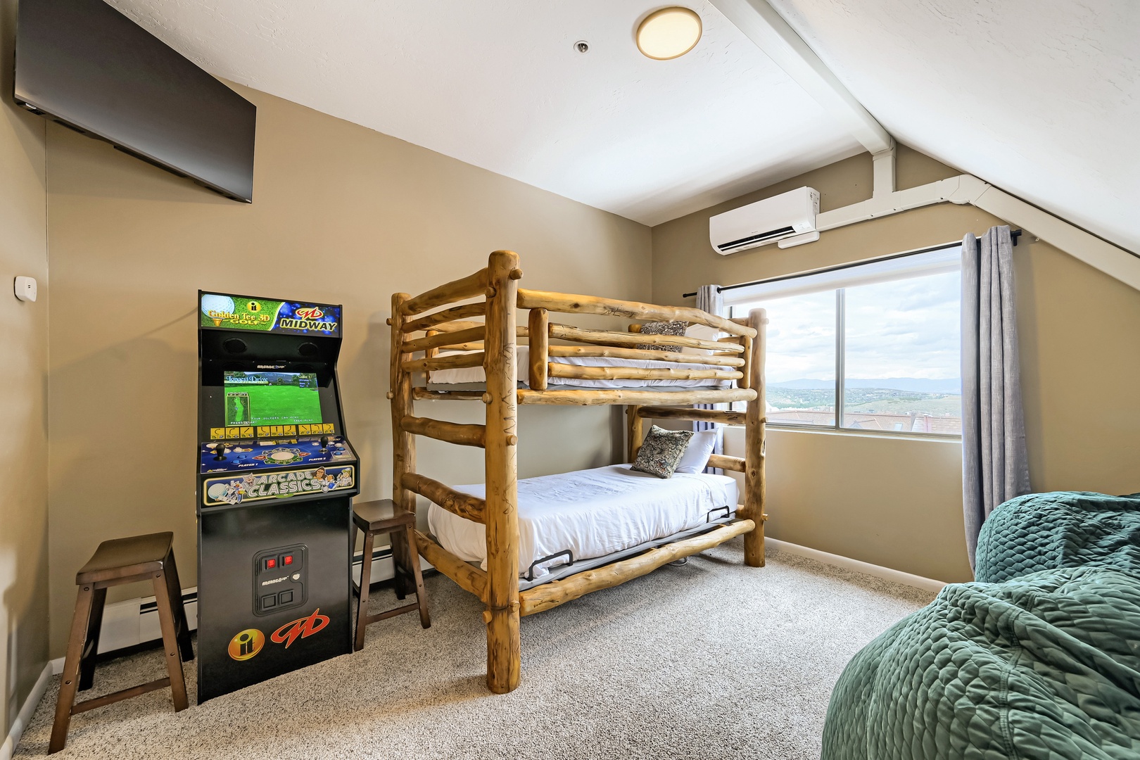 Your family will love this cozy bedroom with rustic bunk beds, an arcade game for entertainment, and a window framing scenic lake views—perfect for restful nights and fun-filled days.