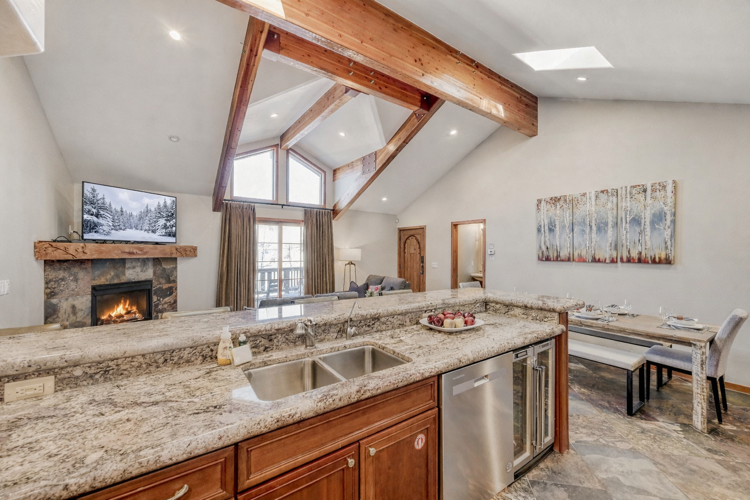 Your open-concept kitchen flows seamlessly into the cozy living space, where warm wood beams frame mountain views and a crackling fireplace awaits.