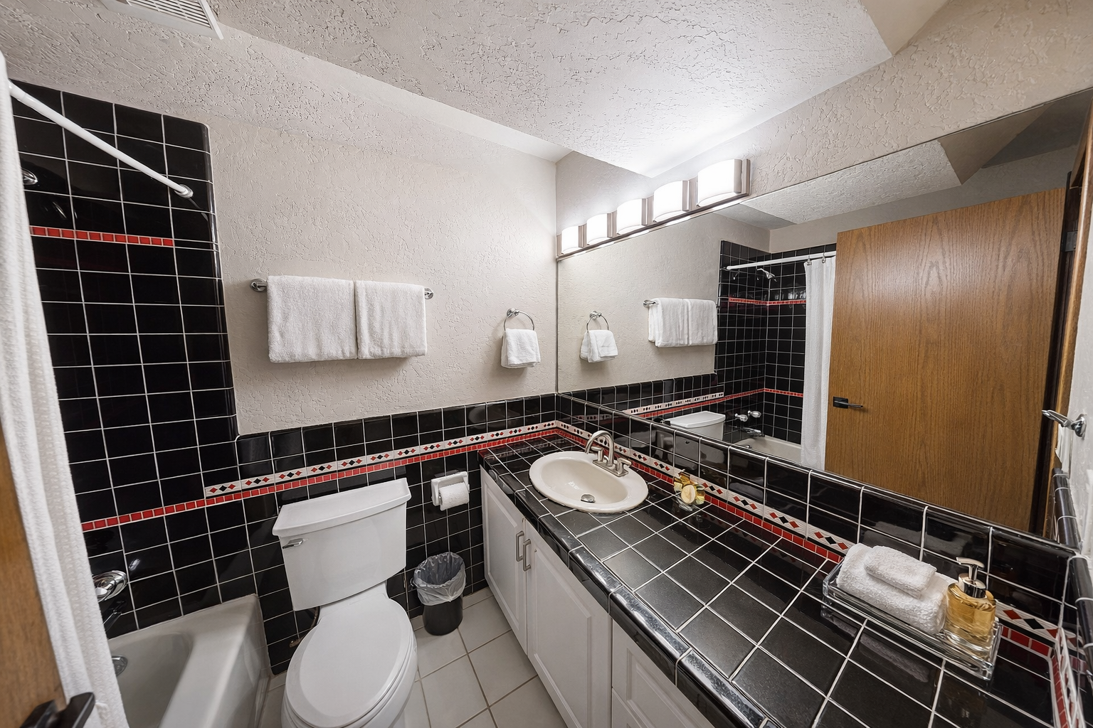 Step into your private bathroom featuring striking black tiles with red accents, fresh towels, and thoughtful amenities awaiting your arrival.