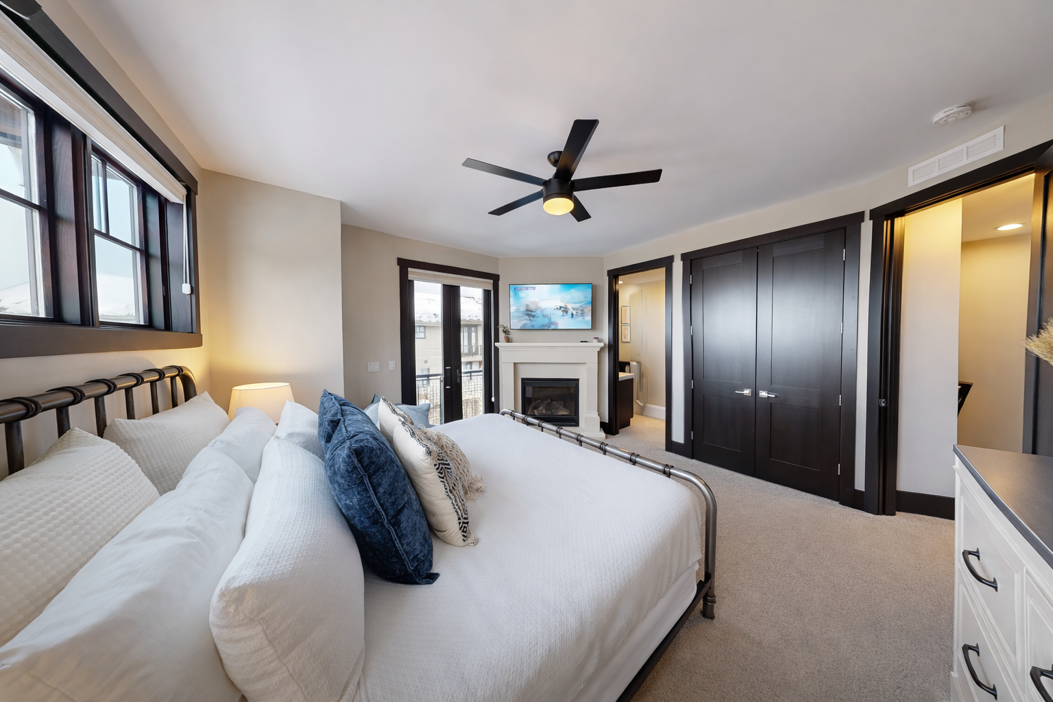 Relax in this bright master suite featuring a plush king bed and a cozy fireplace. Large windows and a private balcony offer serene views for a perfect mountain retreat.