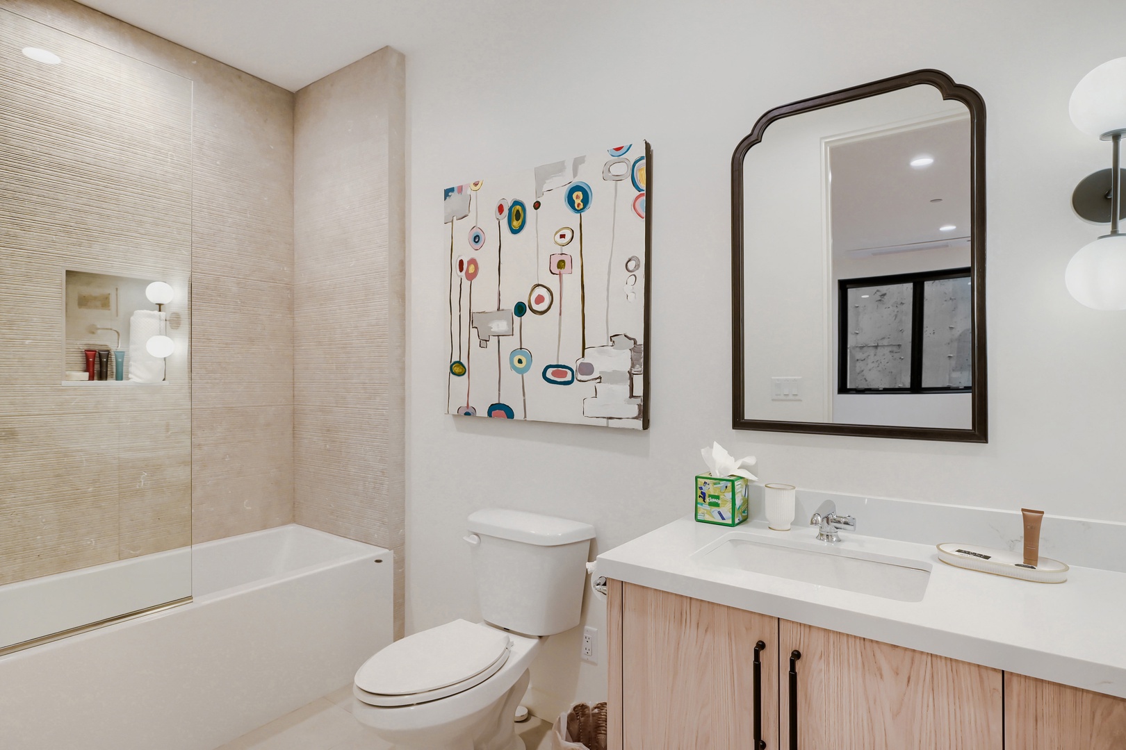 Step into your bright, modern bathroom featuring a full tub, clean lines, and artistic touches. Fresh towels and a well-lit vanity await to start your day right.
