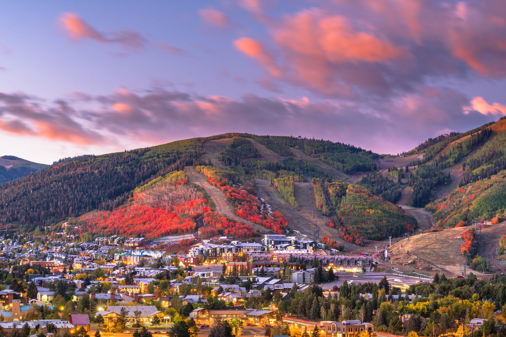 Mountain town nestled in colorful autumn foliage beneath dramatic sunset skies, showcasing the stunning natural beauty of the surrounding area.