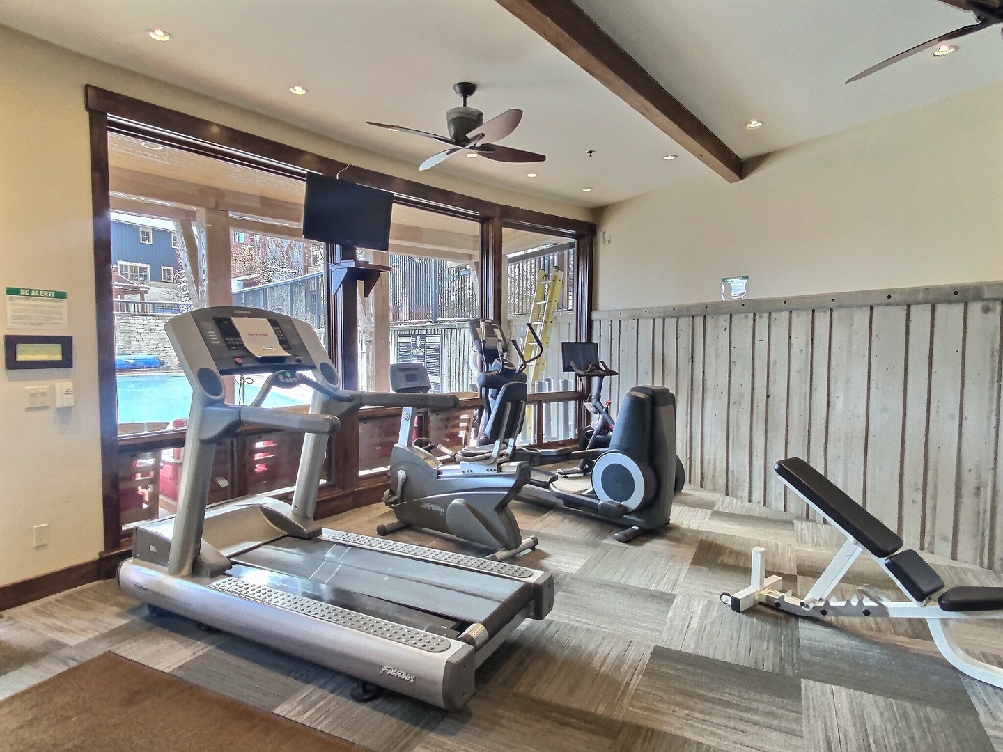 Stay on track with your fitness goals in this well-equipped gym featuring treadmills, ellipticals, weights, and a mounted screen for guided workouts—all with scenic pool views.