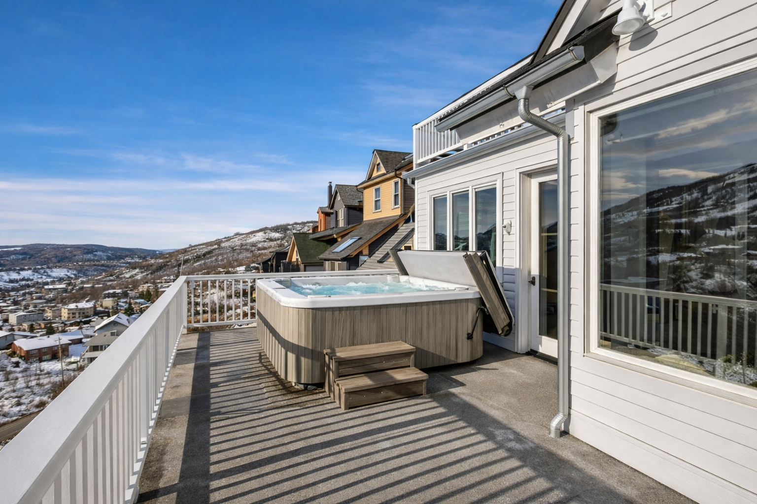 Mountain views and snowy landscape surround this elevated deck featuring a private hot tub for year-round relaxation.