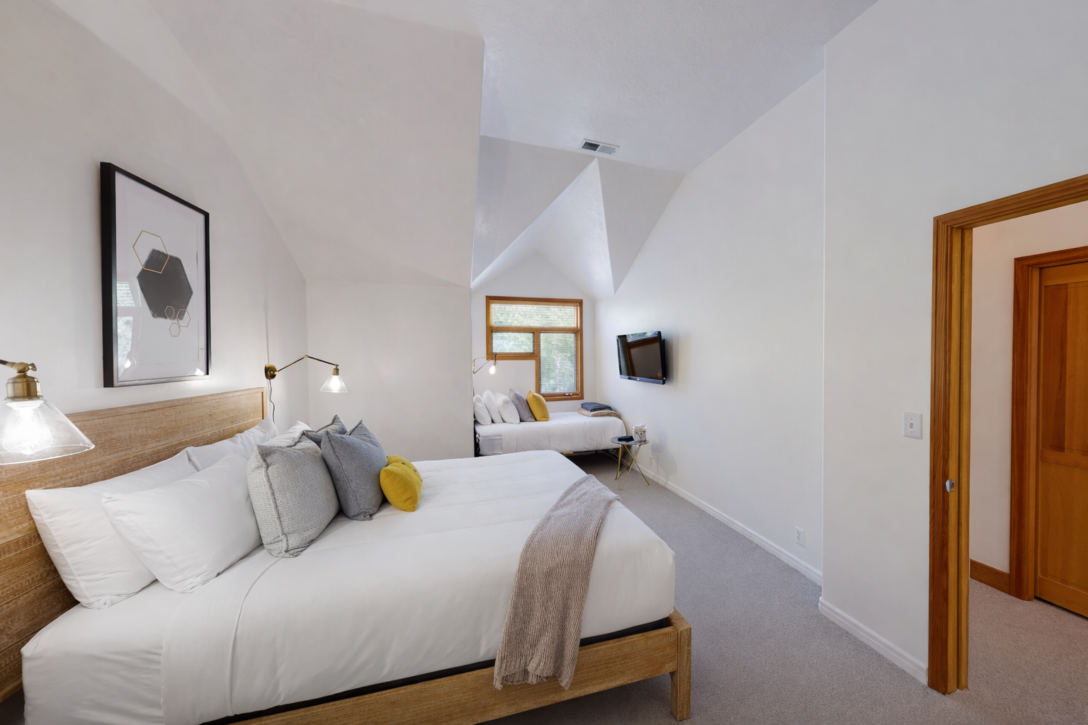 Discover tranquility in this bright, minimalist bedroom featuring a comfortable natural wood bed and a cozy daybed. Large windows offer serene views of the outdoors.