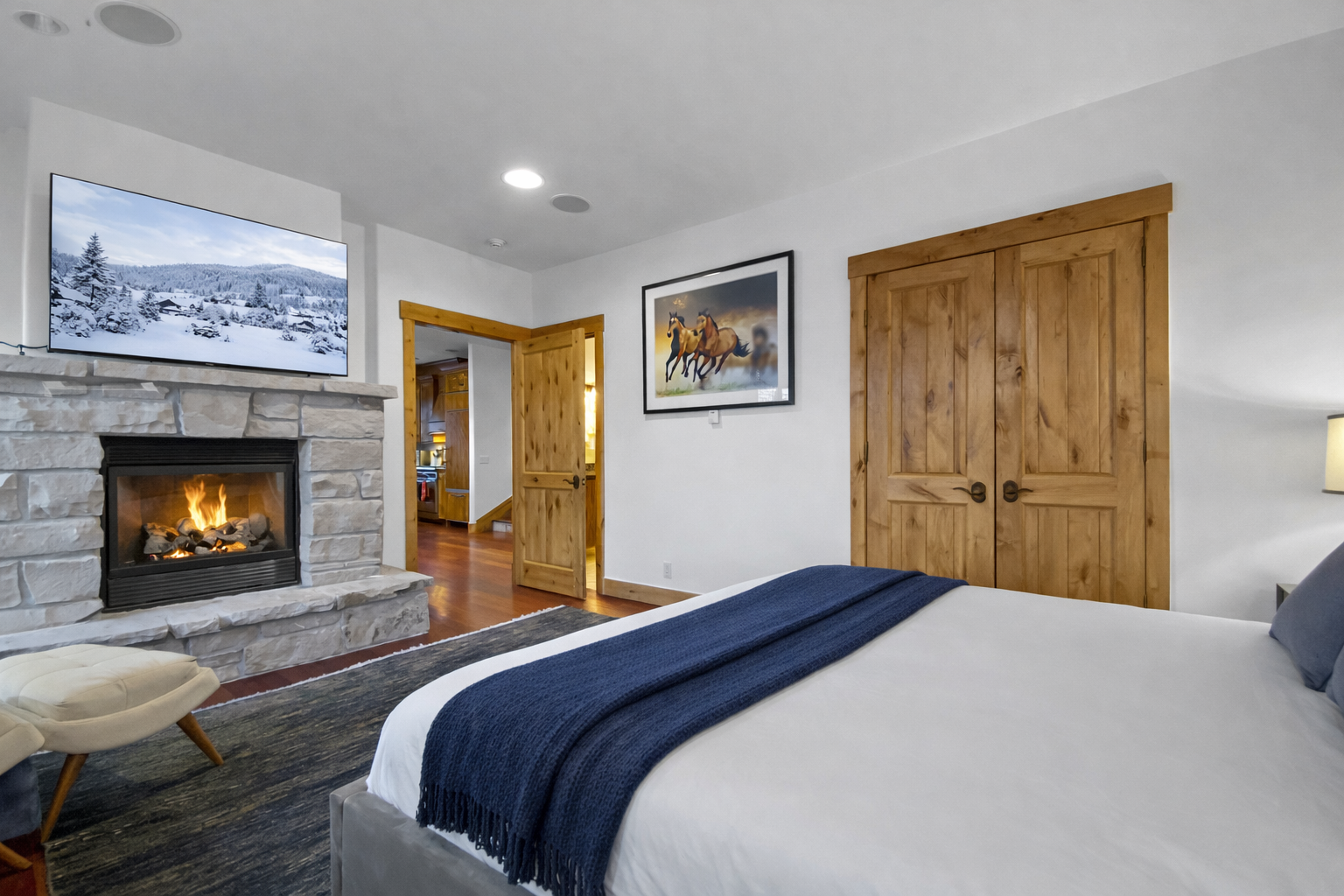 Retreat to this cozy bedroom featuring a inviting fireplace for warmth and ambiance. Relax in comfort with a large TV and natural wood doors adding a rustic touch.