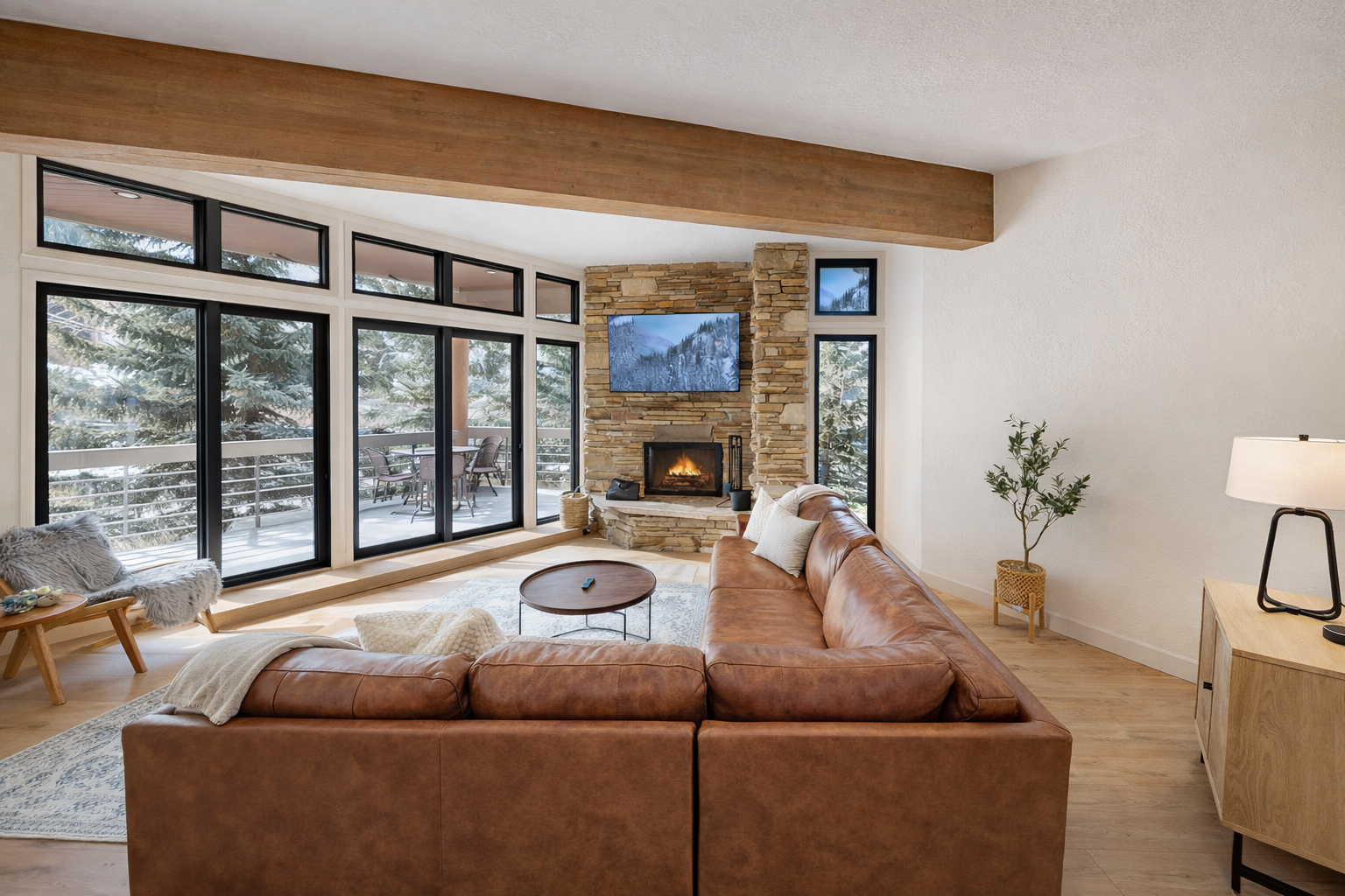Sink into the warm leather sofa and feel the sunlight streaming through floor-to-ceiling windows as exposed beams create cozy charm above.