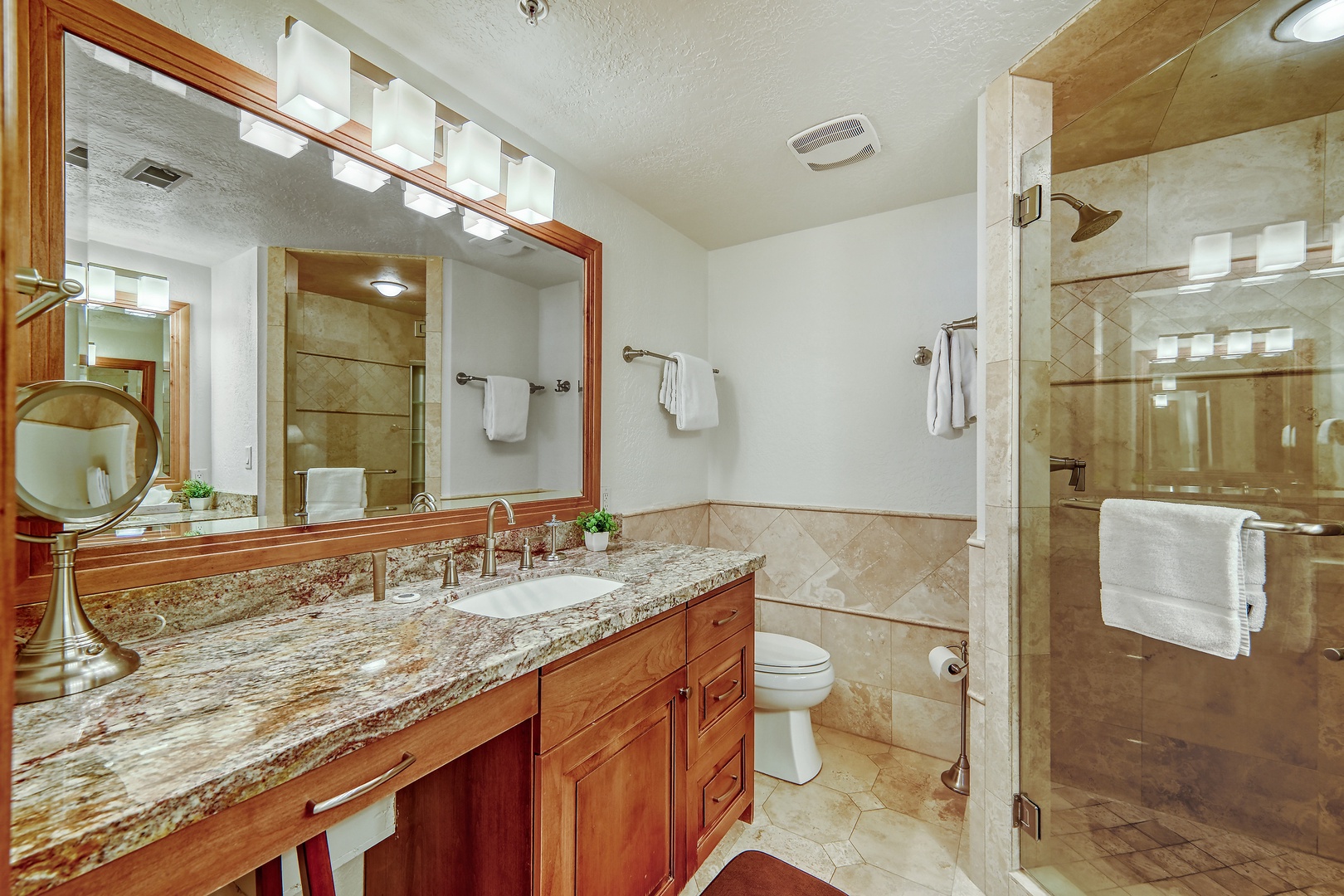 Step into your elegant bathroom featuring granite countertops, rich wood cabinetry, and a spacious glass-enclosed shower for your relaxing retreat.