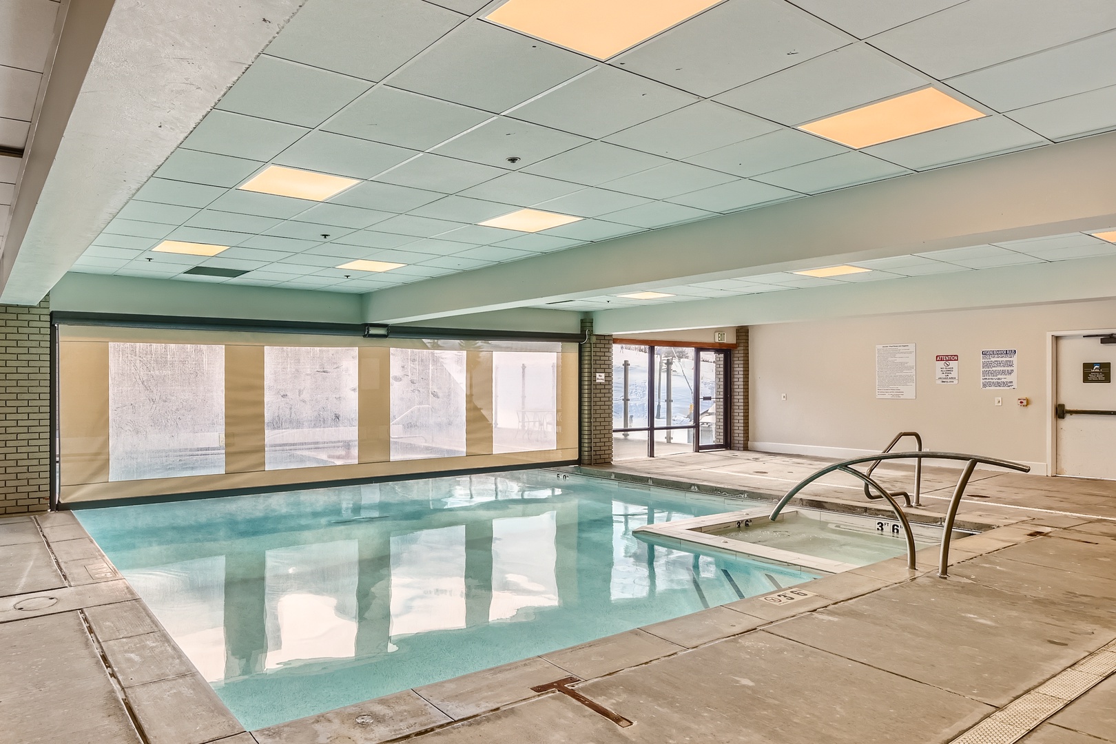 The indoor pool offers a refreshing retreat with easy entry access and abundant natural light streaming through expansive windows, perfect for a relaxing swim anytime.