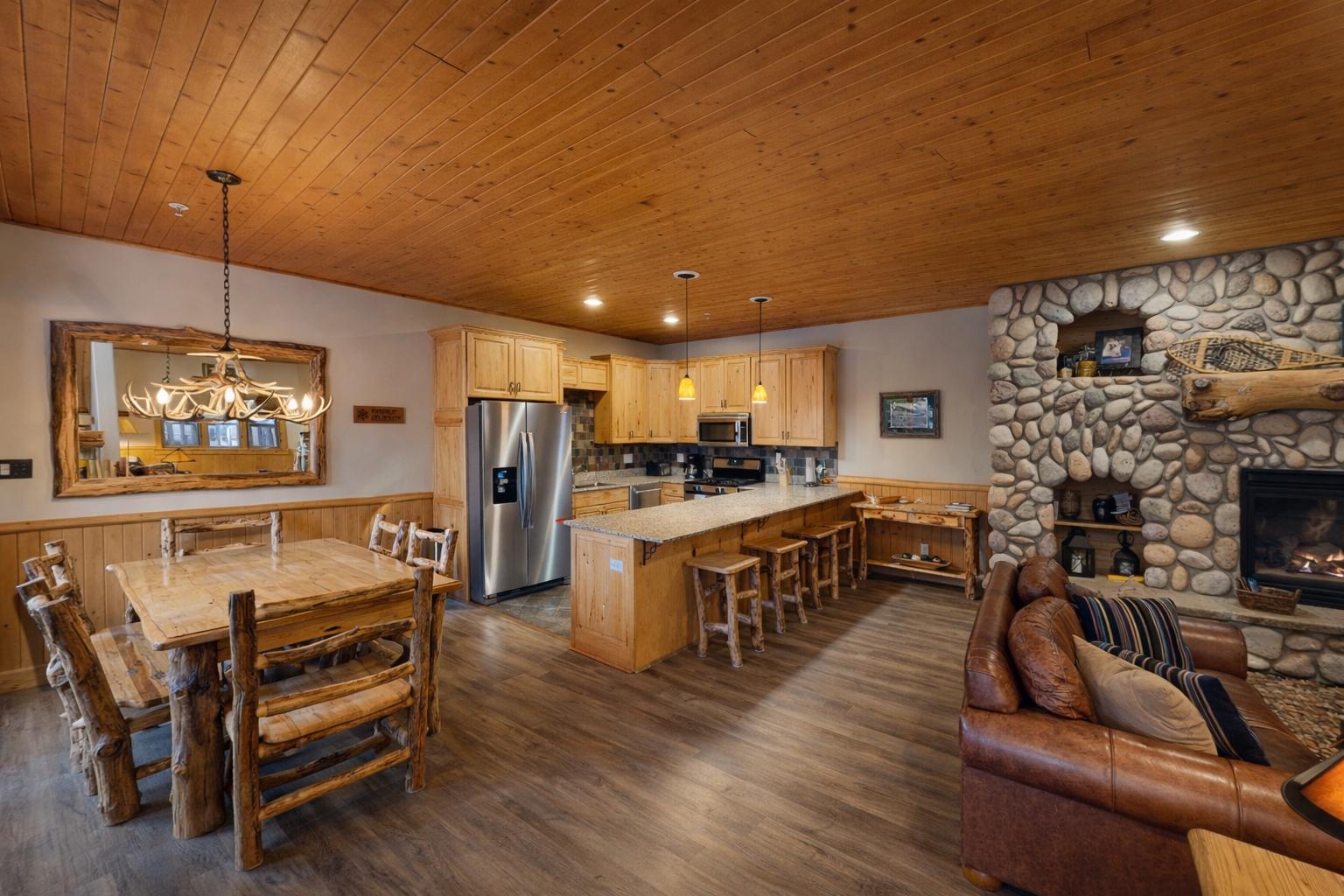 Warm wood ceiling and rustic stone fireplace create your cozy mountain escape, where kitchen, dining, and living spaces flow together perfectly.