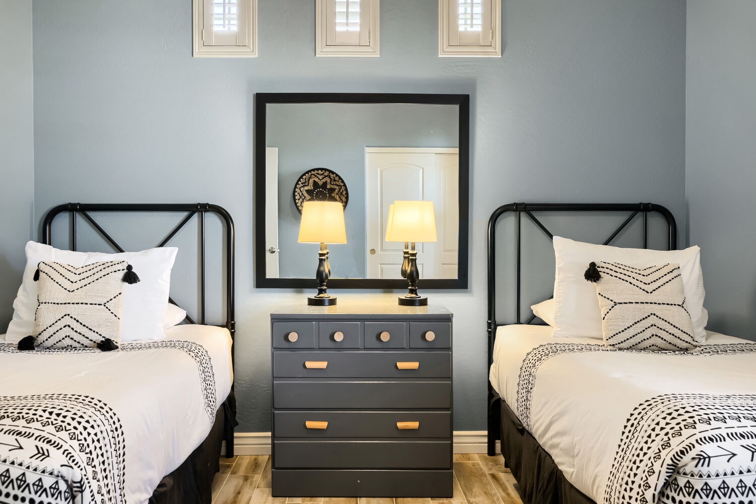 Relax in a chic bedroom with twin beds, soft linens, warm bedside lighting, and serene blue-gray walls that invite restful nights and peaceful mornings.