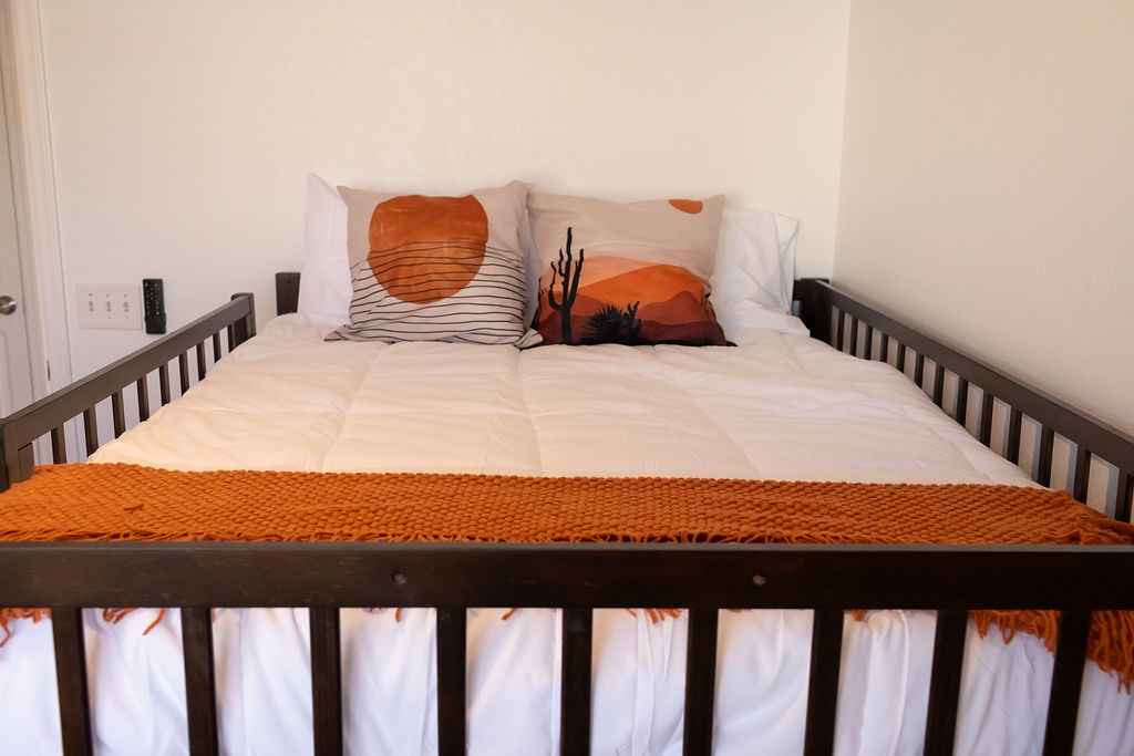 Cozy desert-themed bed awaits with artistic pillows and warm orange accents for your peaceful retreat.