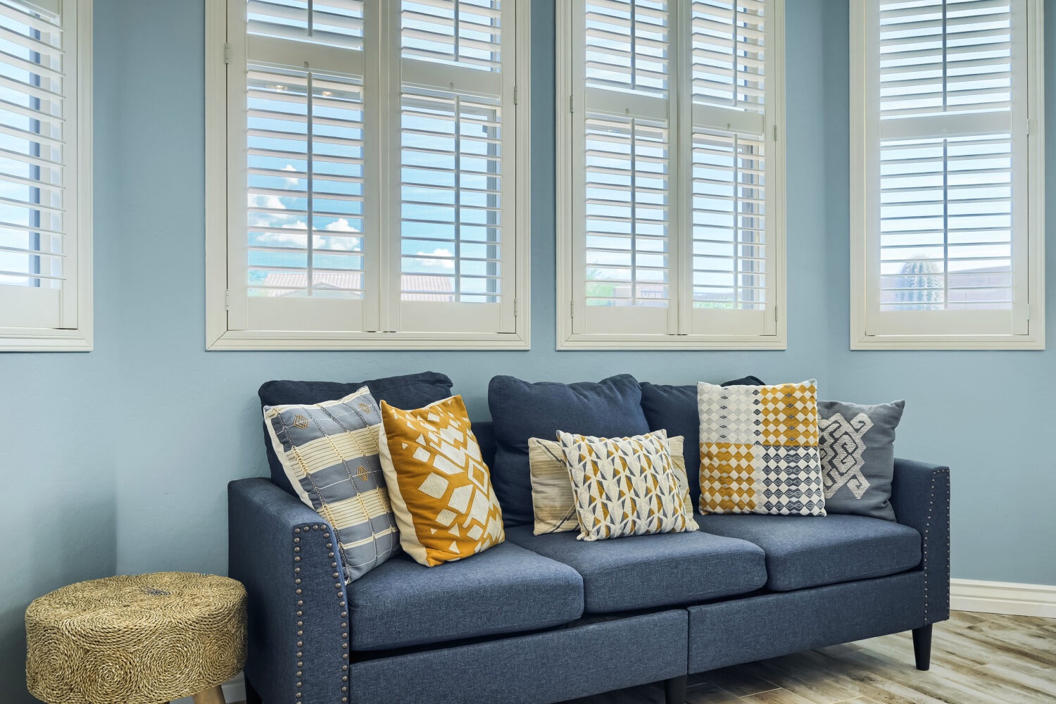 Settle into your stylish living room, where crisp white shutters frame calming blue walls and a charming navy sofa with patterned mustard-and-gray pillows invites you to unwind.