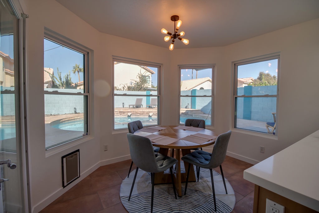 Your bright breakfast nook overlooks the sparkling pool, where morning coffee feels extra special with those panoramic windows and stylish chandelier overhead.