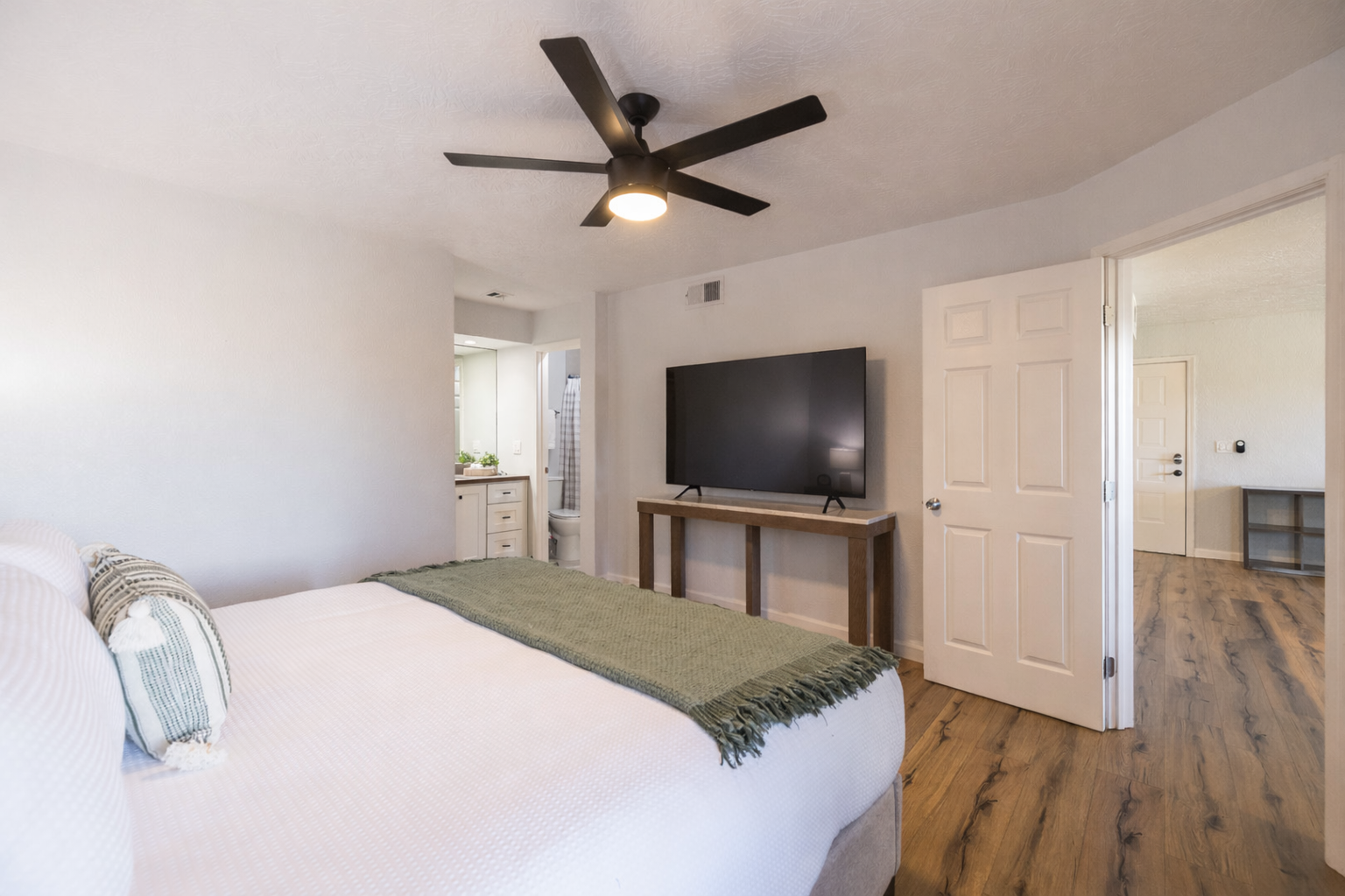 Relax in your spacious bedroom with modern ceiling fan, flat-screen TV, and beautiful hardwood floors creating the perfect retreat.