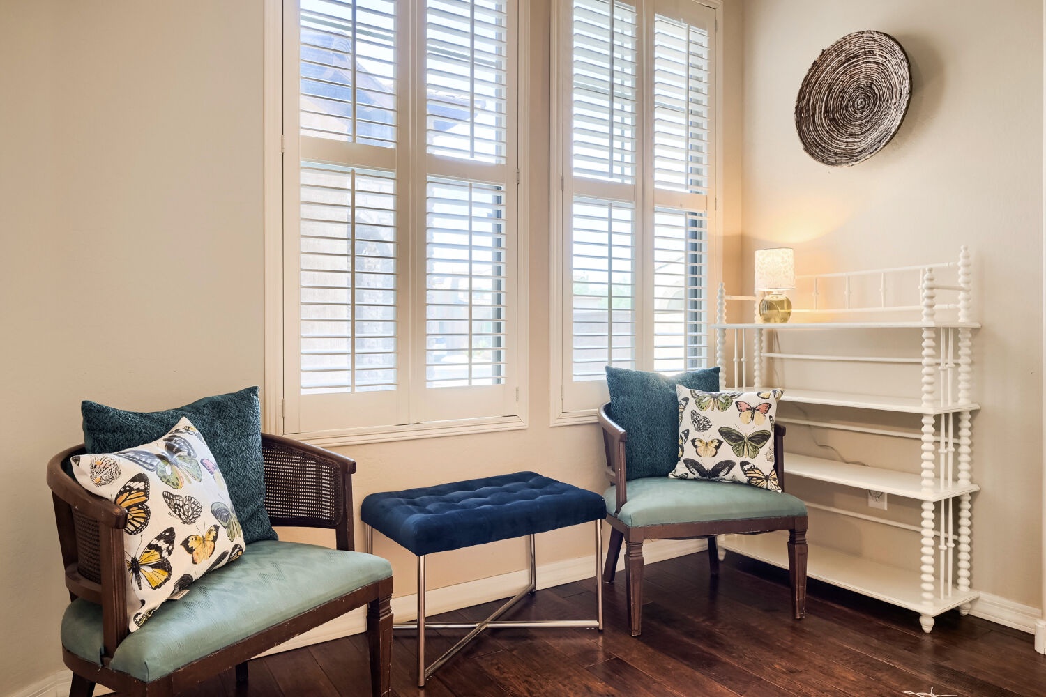 Settle into your tranquil reading nook, where plantation shutters filter soft daylight and inviting chairs with butterfly-print pillows create your perfect spot to unwind.