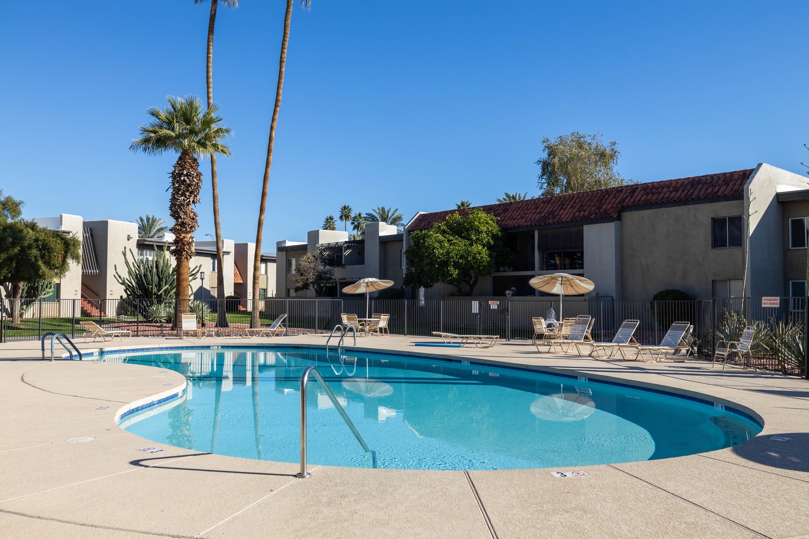 Sparkling blue heated community pool with comfortable loungers under desert sunshine.