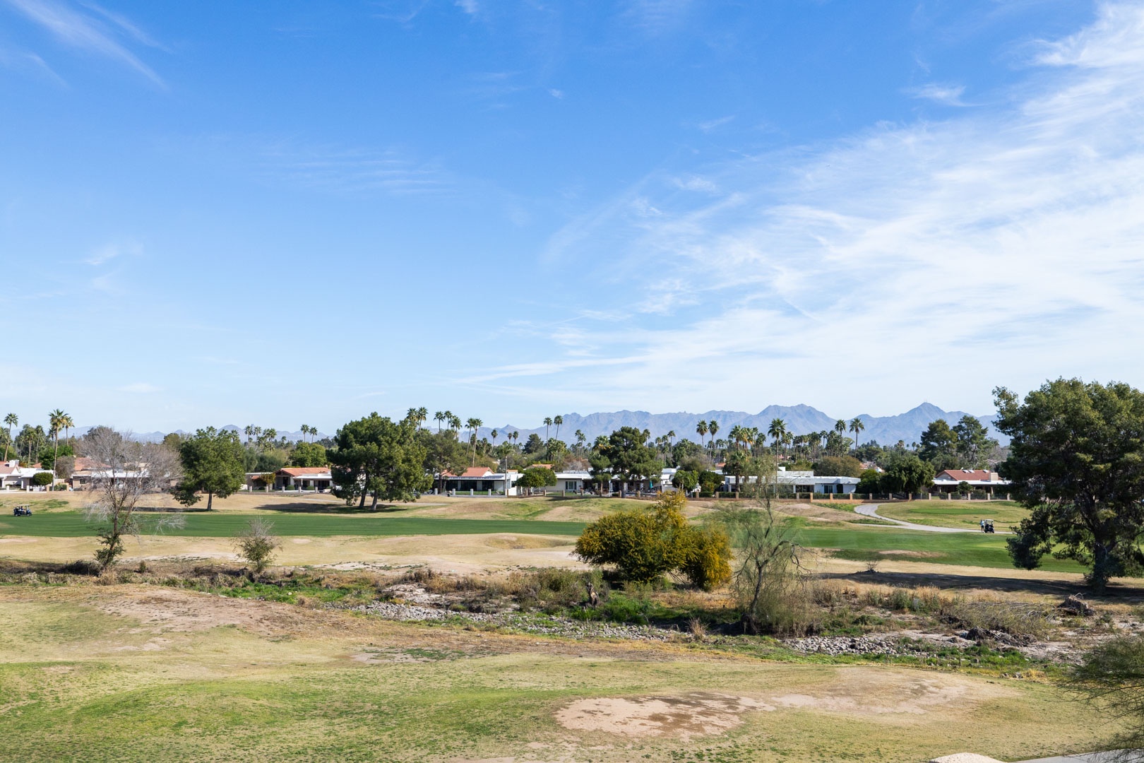 Desert golf course surrounded by residential community with mountain backdrop and palm trees dotting the landscape.