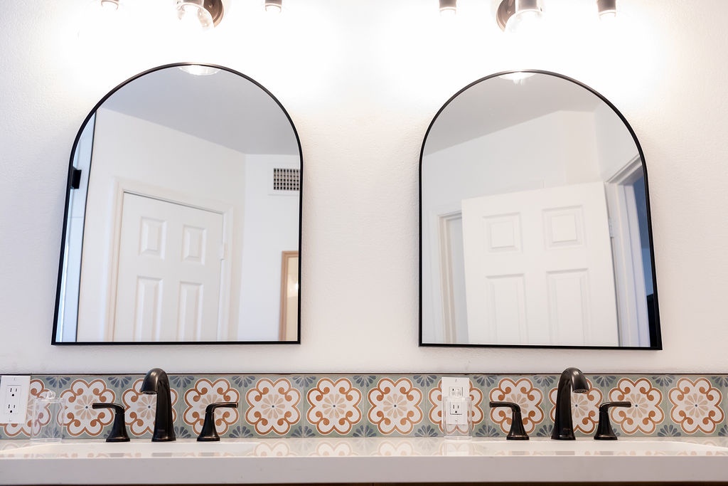 Your elegant double vanity features stylish arch mirrors and decorative tile backsplash, creating a sophisticated morning routine space.