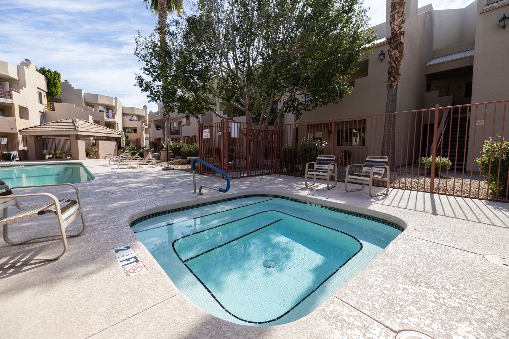 Community hot tub and pool area surrounded by mature trees and comfortable seating in a well-maintained residential complex.