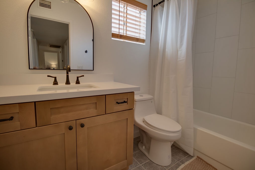 Step into your private sanctuary with a soaking tub, spacious vanity, and natural light streaming through wooden blinds for your perfect morning routine.