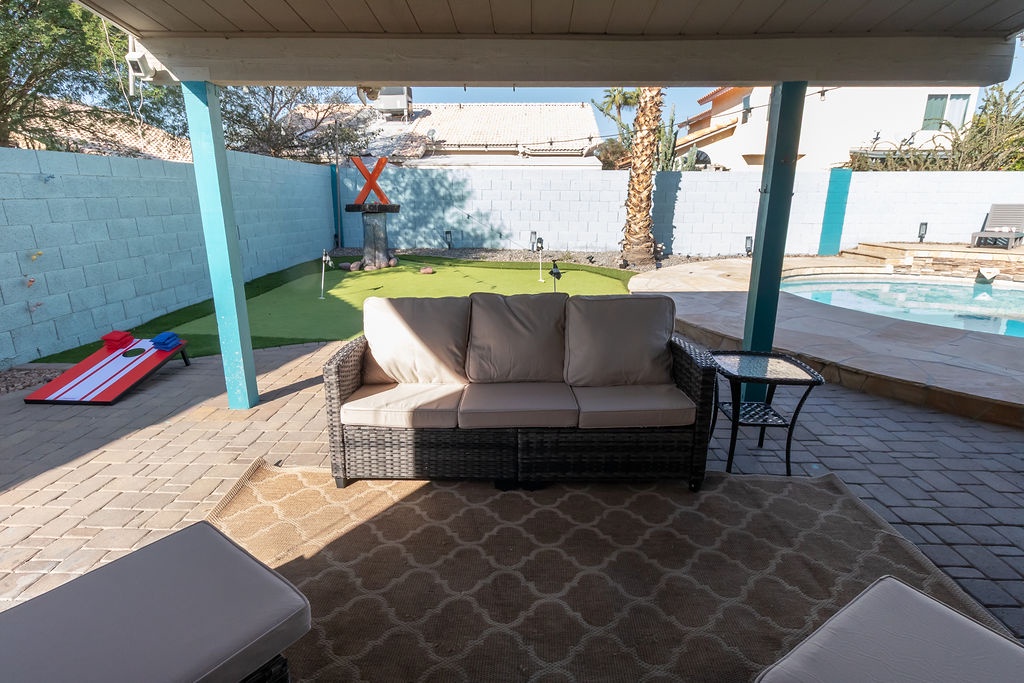 Your covered outdoor lounge offers shaded comfort beside the pool, with wicker seating and putting green for perfect relaxation.