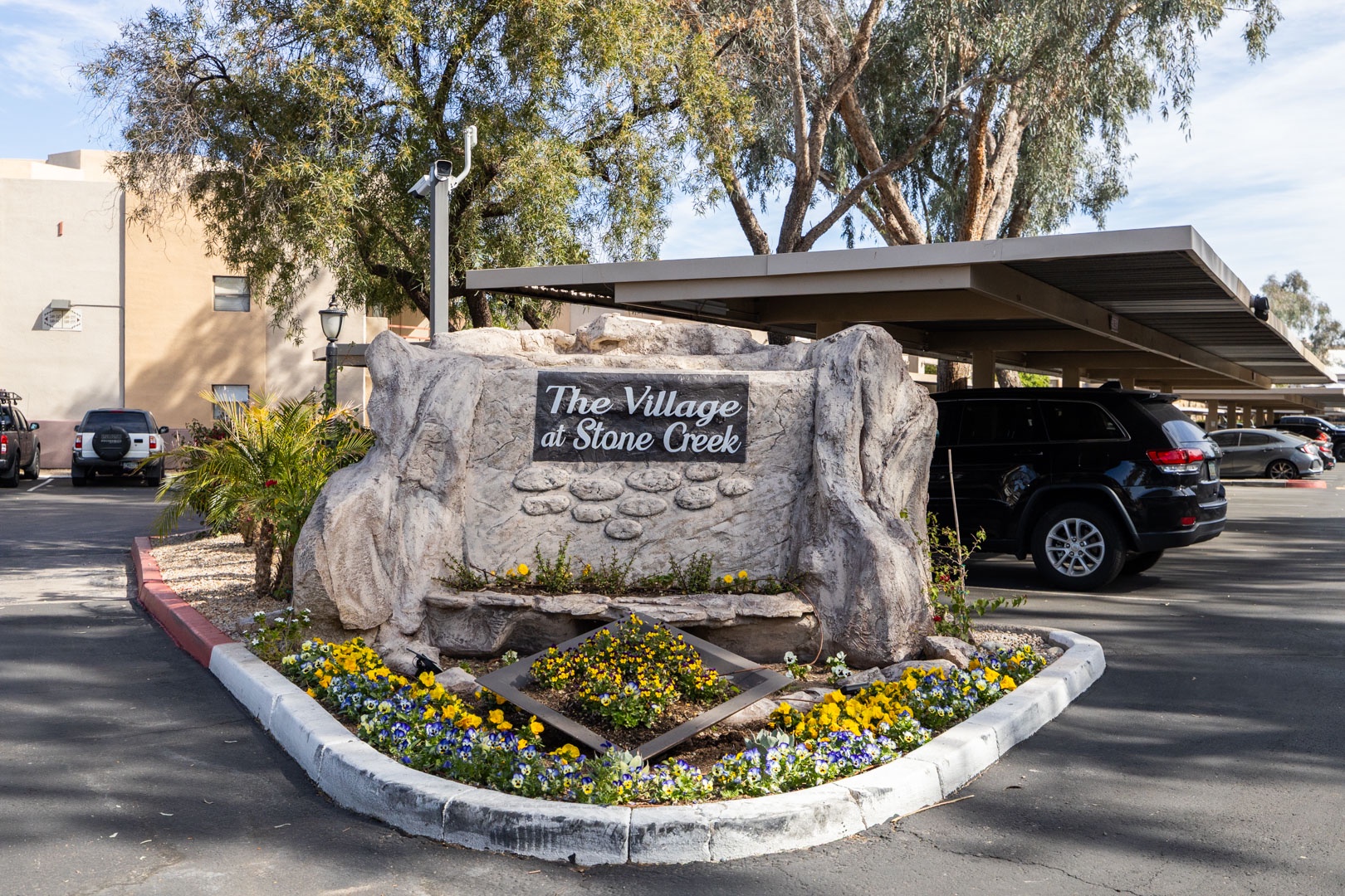 Stone Creek Village entrance sign welcomes visitors with landscaped gardens and covered parking facilities.