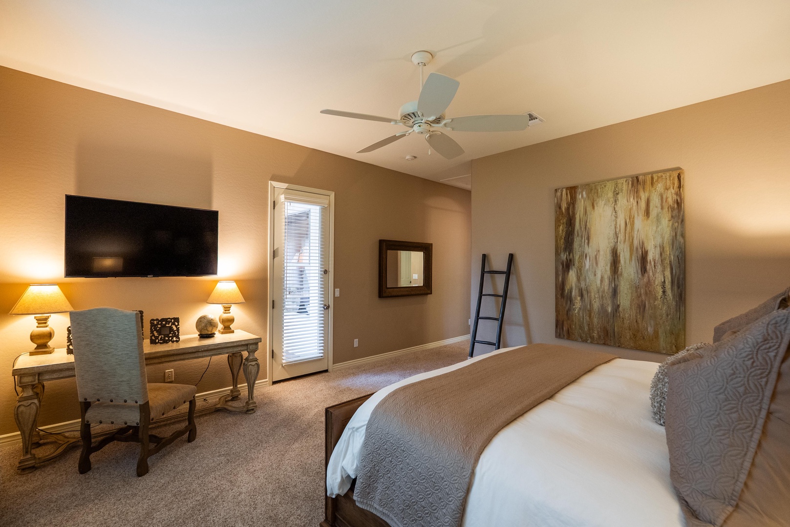 King primary suite with TV, desk and patio access