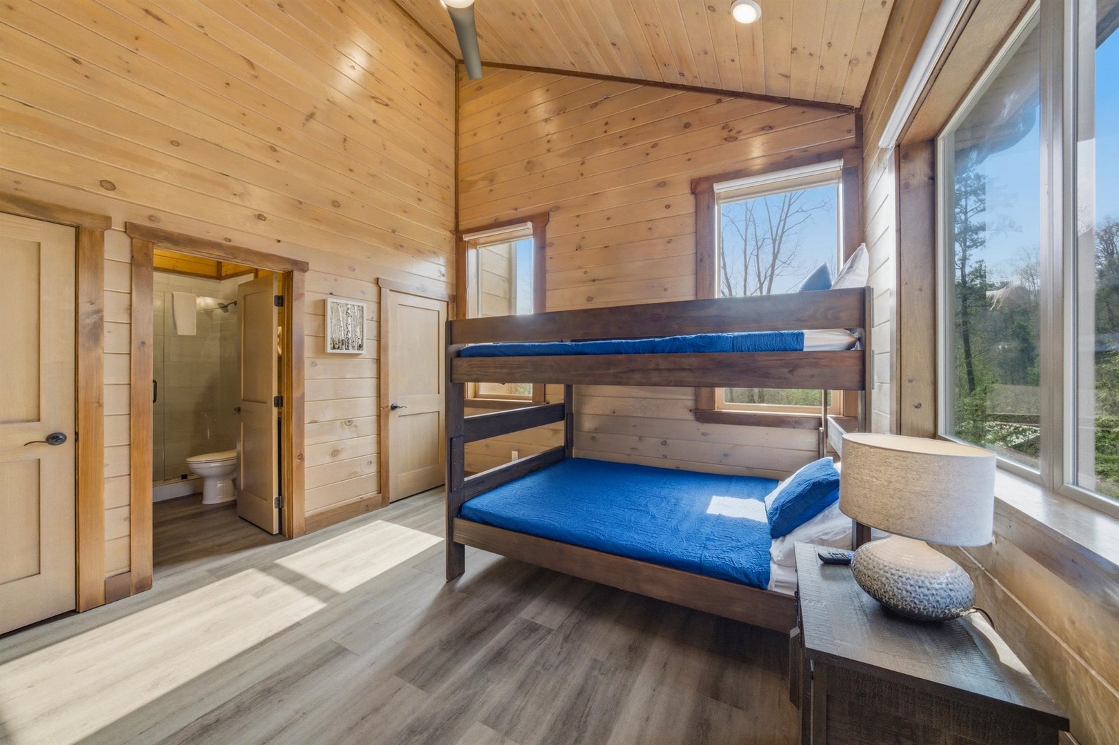 Cozy wooden bunk bed room with bright windows offering forest views and private bathroom access.