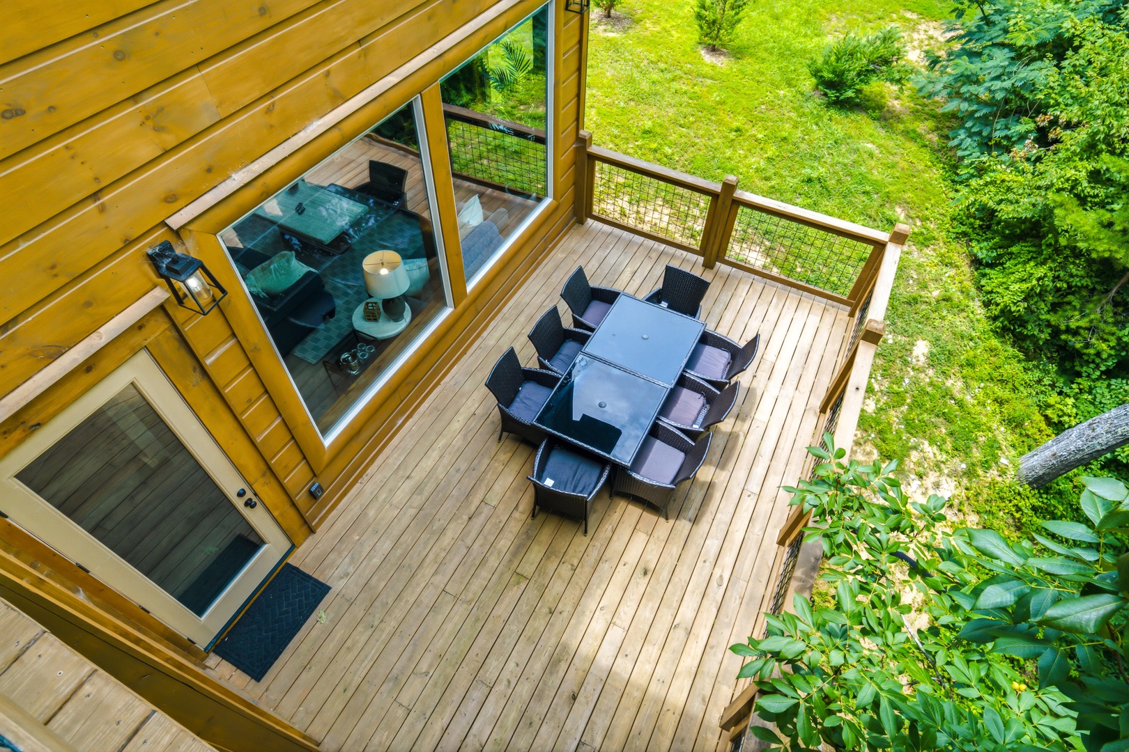 Aerial view of a spacious wooden deck with outdoor dining for eight, overlooking a lush garden surrounded by evergreens and vibrant greenery—perfect for relaxing meals outdoors.