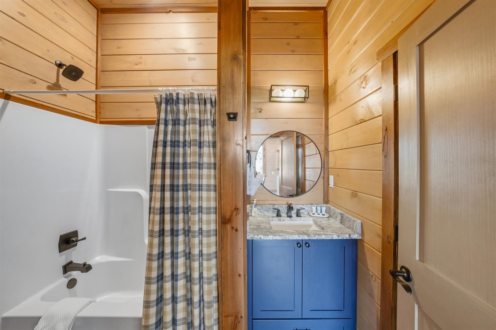 Refresh in your charming cabin bathroom with warm wood walls, vintage blue vanity, and clean shower-tub combo.