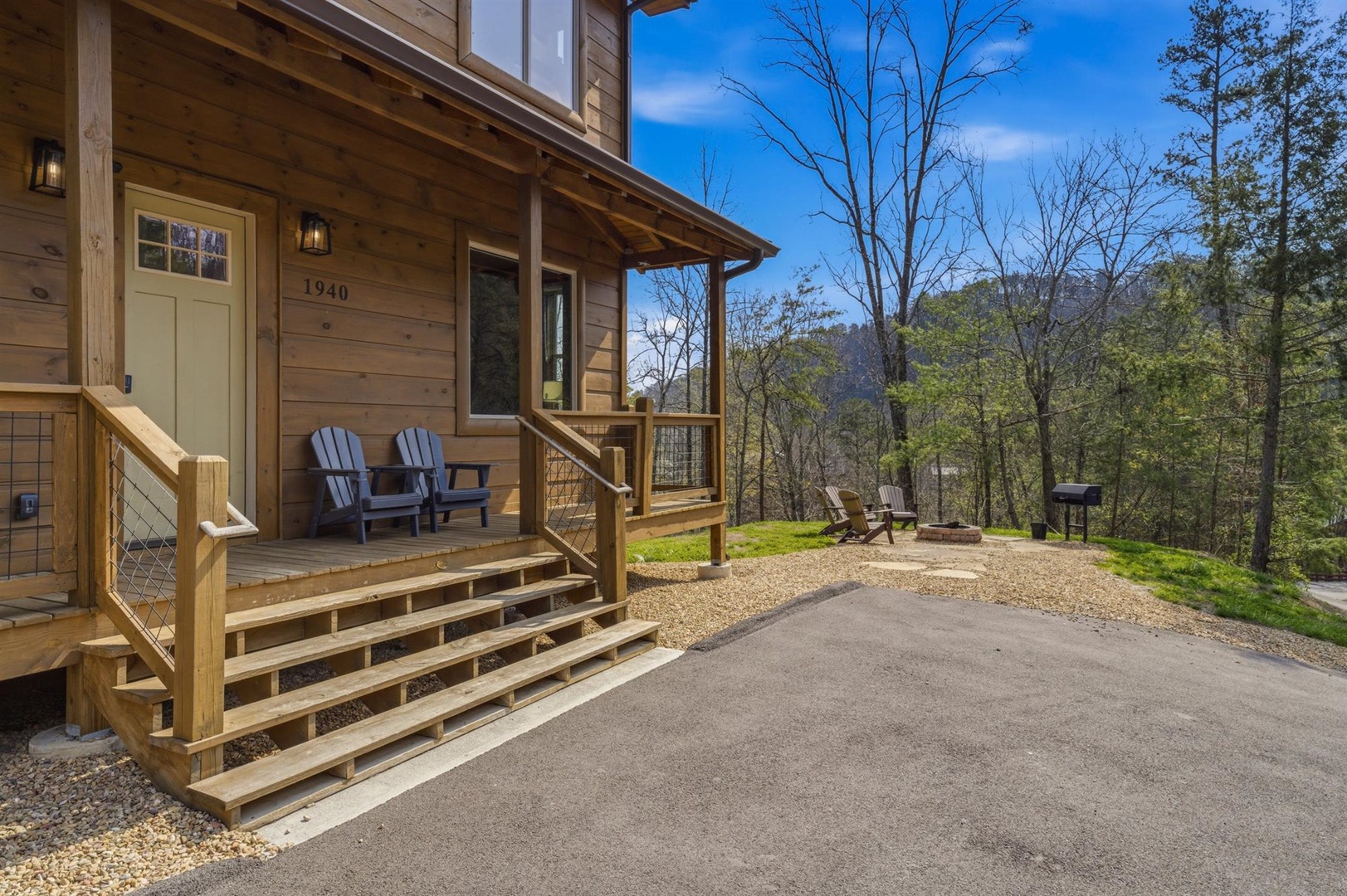 Charming cabin facade with covered porch and mountain forest setting, complete with parking and outdoor seating areas.