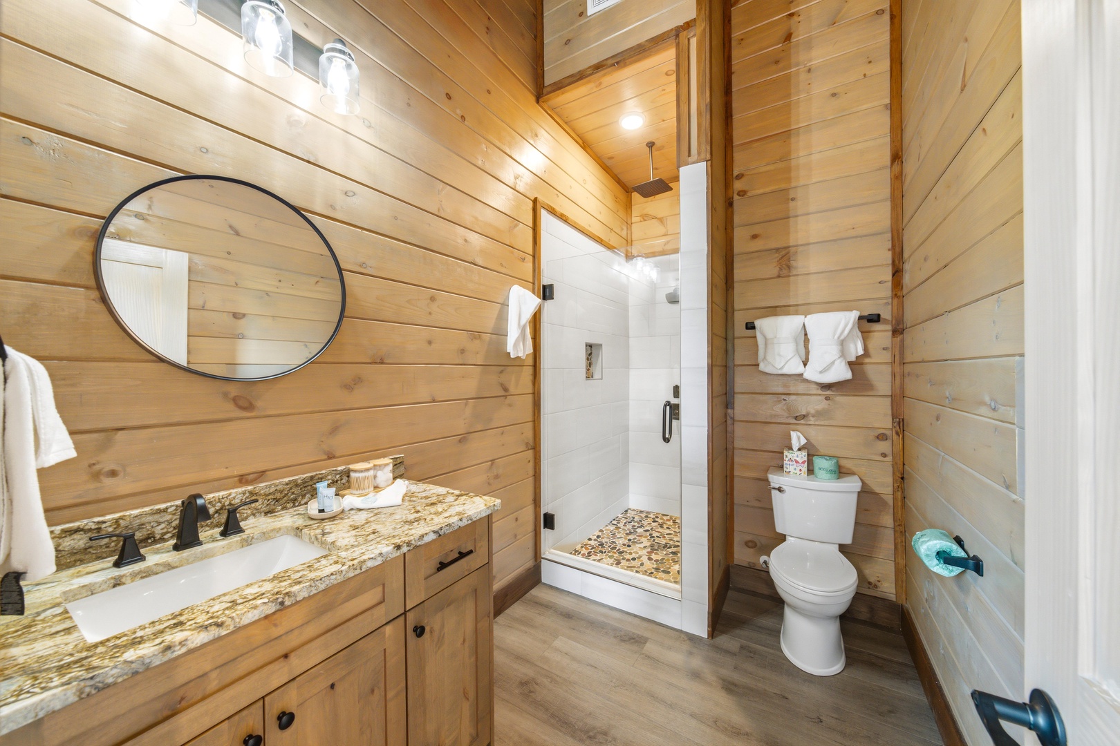 Your private bathroom feels like a warm retreat, wrapped in natural wood and featuring a sleek vanity with granite countertop, walk-in shower, and fresh white towels.