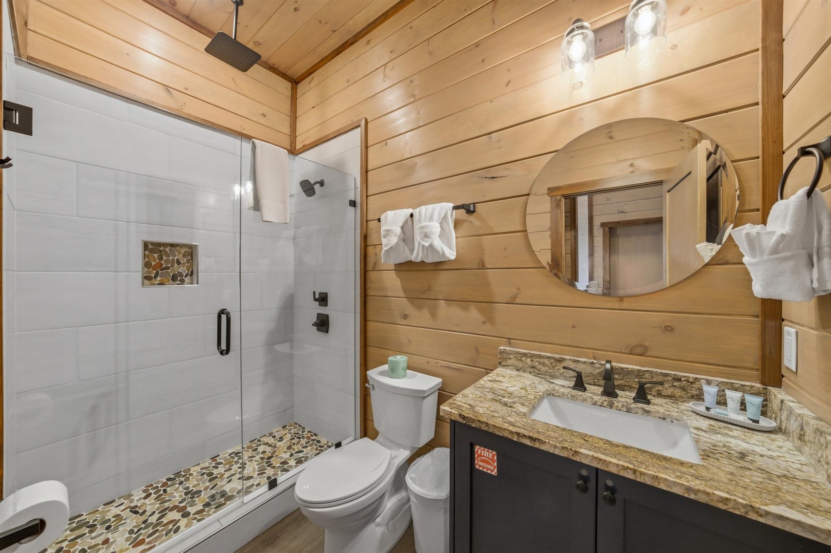 Step into your rustic-chic bathroom with warm wood walls, elegant granite counters, and a spacious glass shower with beautiful stone accents.