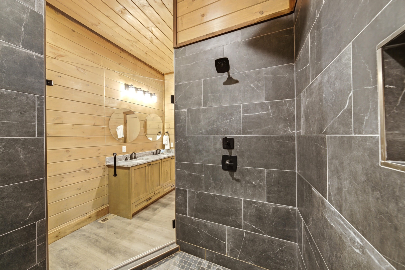 Step into a beautifully designed bathroom where modern elegance meets rustic charm. The spacious walk-in shower features sleek gray tile, while warm wood accents create a welcoming retreat for your relaxation.