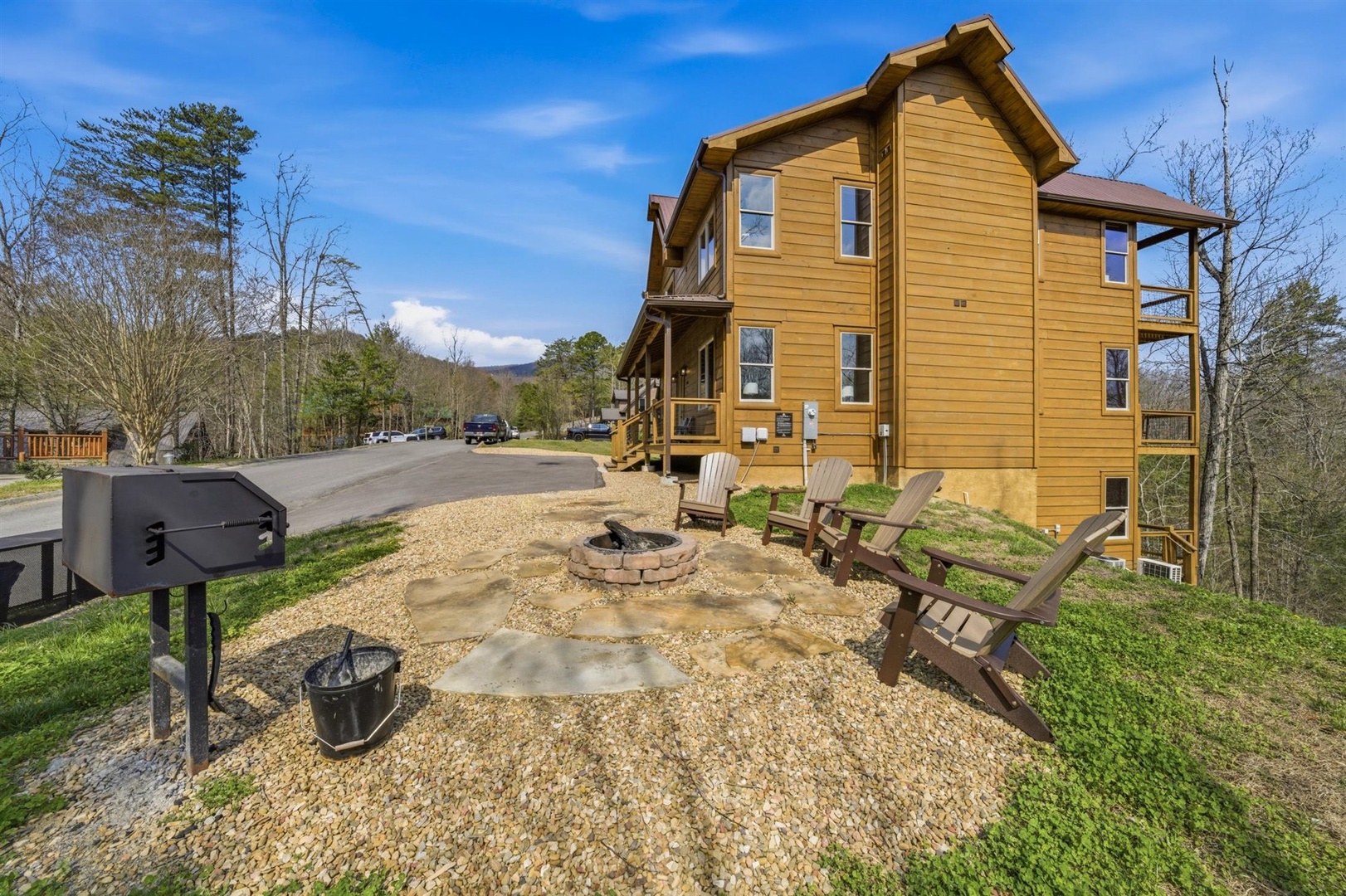 Rustic mountain cabin featuring outdoor fire pit, seating area, and BBQ grill surrounded by natural wooded landscape.